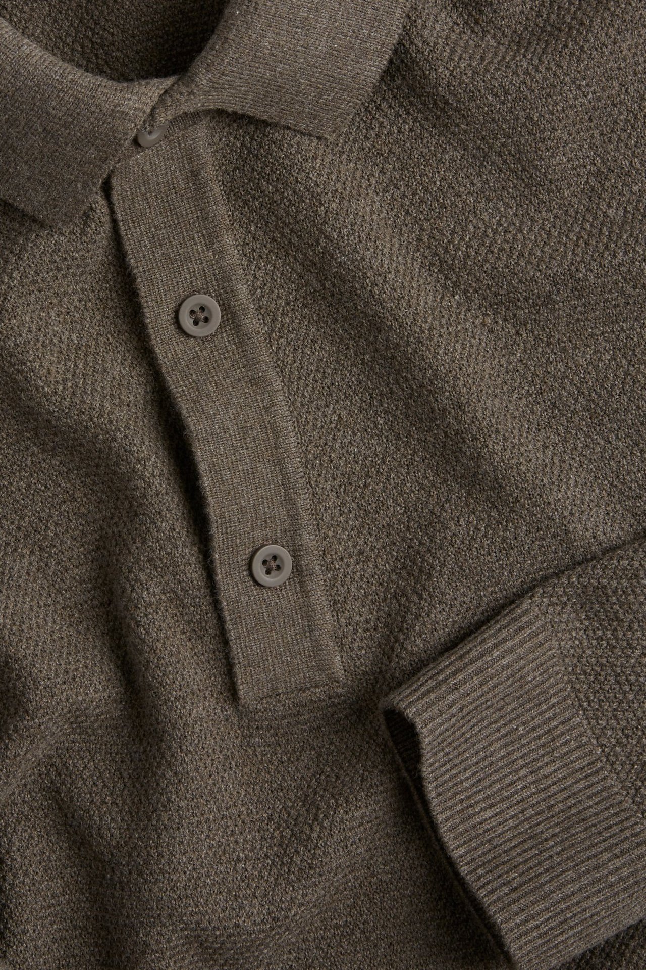 Zbliżenie na brązowy melanżowy sweter z dzianiny o teksturowanym wzorze, kołnierzem, listwą guzikową i ściągaczem.