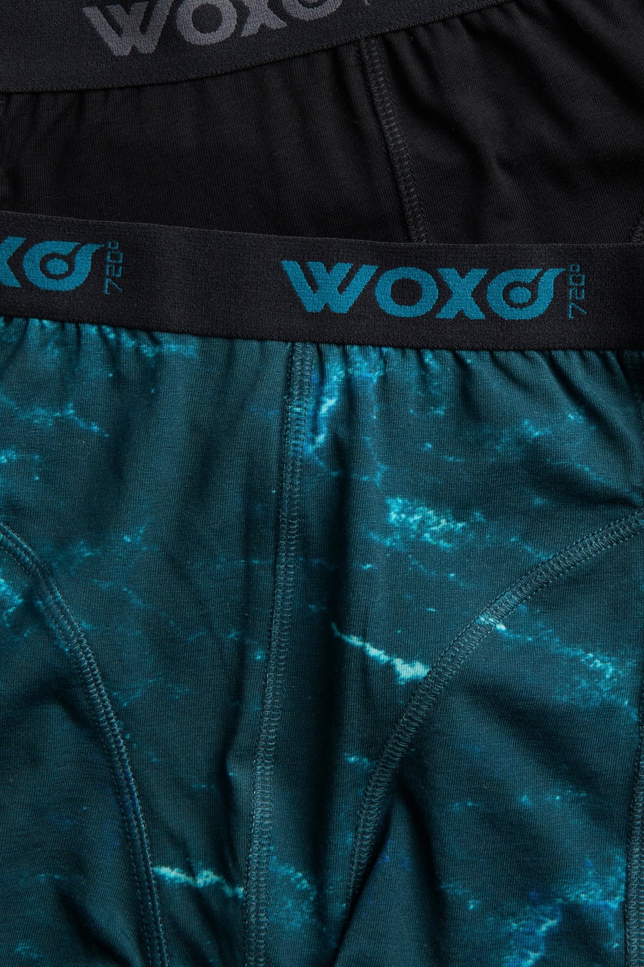 Zbliżenie na zielone wzorzyste bokserki dziecięce z czarnym pasem, ułożone na czarnych bokserkach.