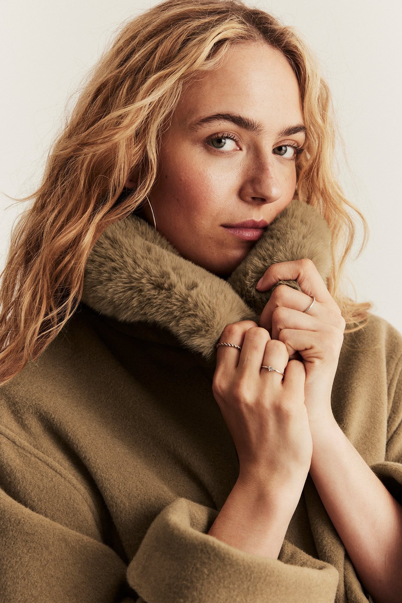 Närbild på kvinna i brun ullblandningskappa med ljusare fuskpälskrage, bärande ringar.