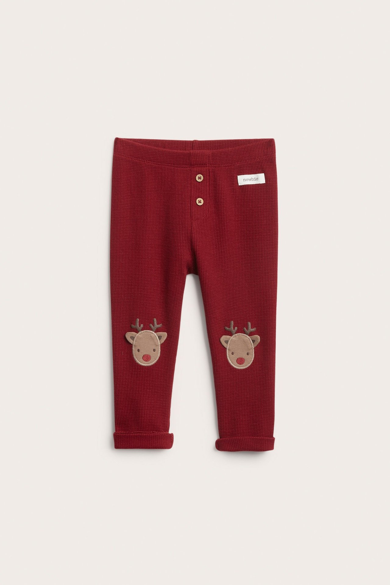 Framifrån: Babyns röda våffelstickade leggings med knappar fram, renapplikationer på knäna och uppvikta muddar.