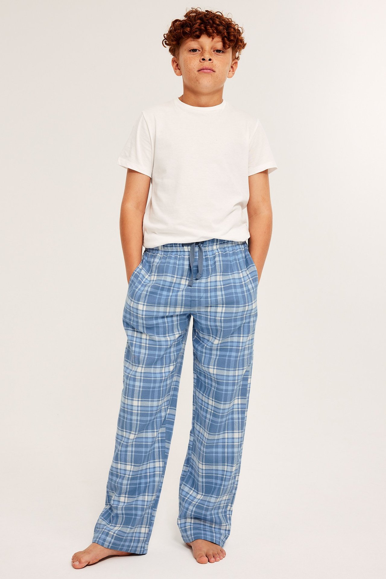 Poika valkoisessa t-paidassa ja sinisissä ruudullisissa lapanakaapissa, joustinvyöt, taskut ja suorat lahkeet.