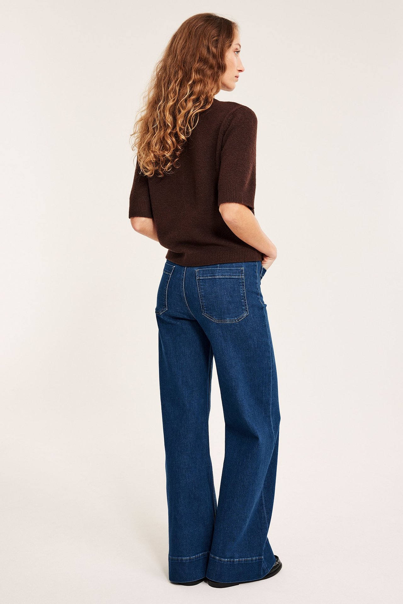 Widok z tyłu kobiety w granatowych szerokich jeansach z wysokim stanem i brązowym swetrze z krótkim rękawem.