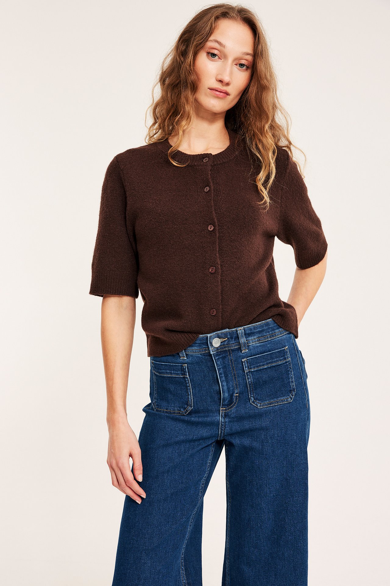 Widok z przodu: Kobieta w niebieskich dżinsach high-waist wide leg z kieszeniami i brązowym krótkim topie.