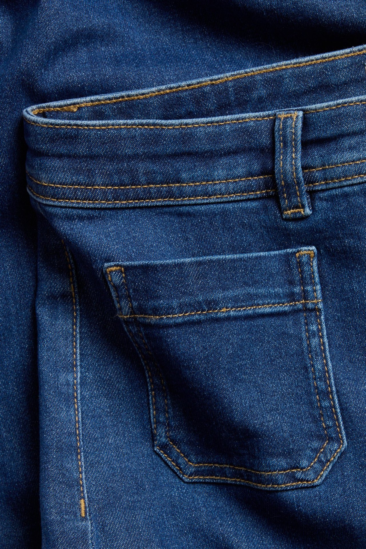 Zbliżenie niebieskich dżinsów wide-leg z denimu, ukazujące tylną kieszeń, pas i pomarańczowe szwy.