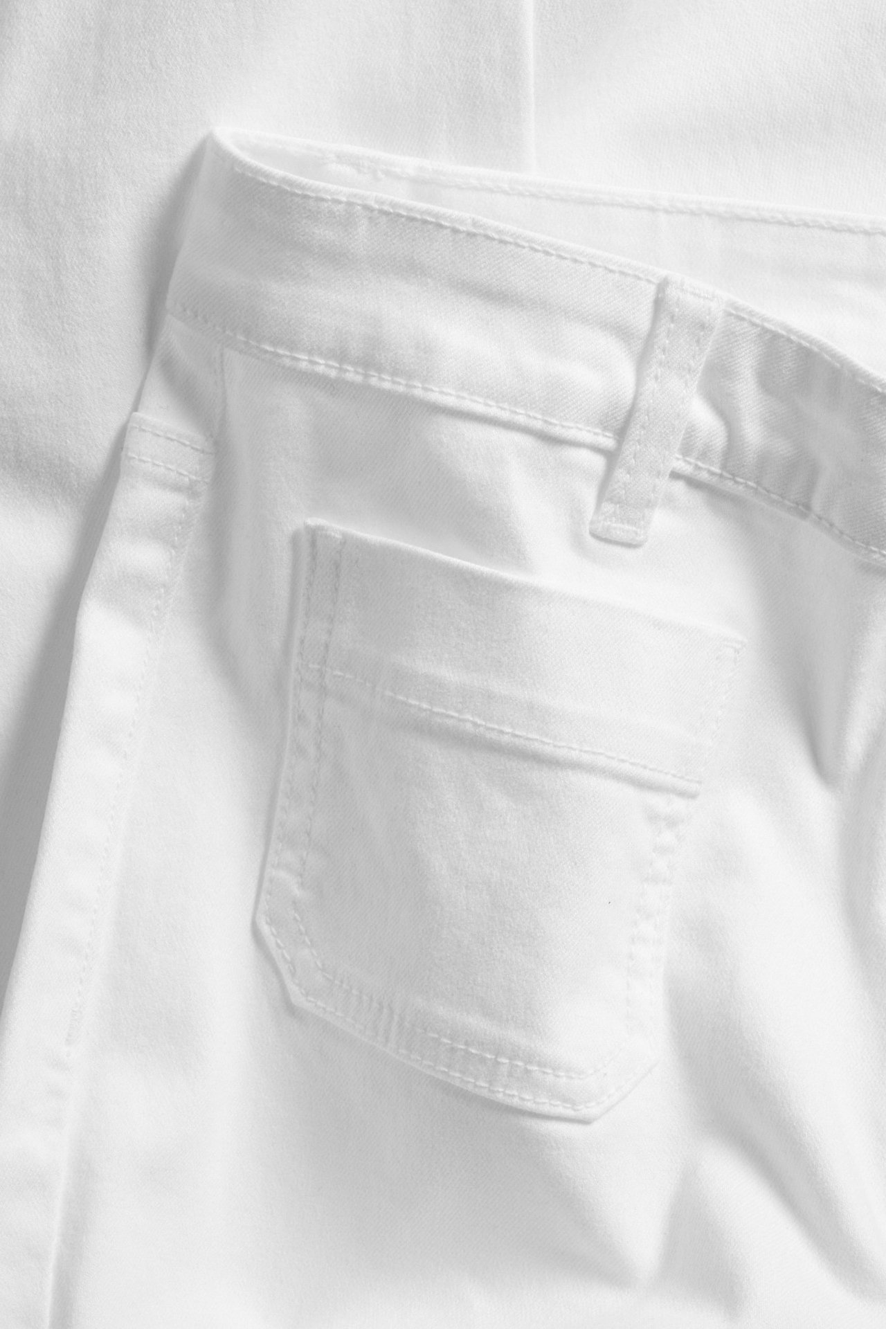 Nærbilde av hvite twilljeans, viser linning, beltestropper og en sydd baklomme.