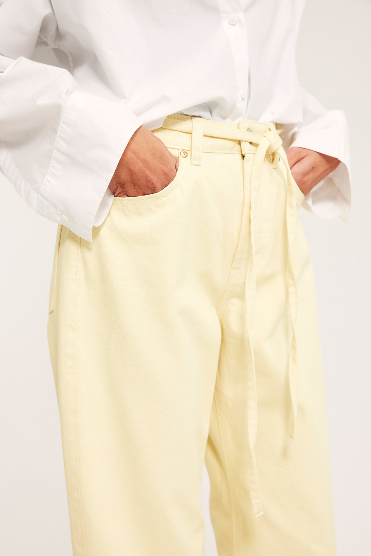 Lähikuva: Nainen yllään vaaleankeltaiset leveälahkeiset farkut, korkea vyötärö, solmuvyö ja valkoinen paita.