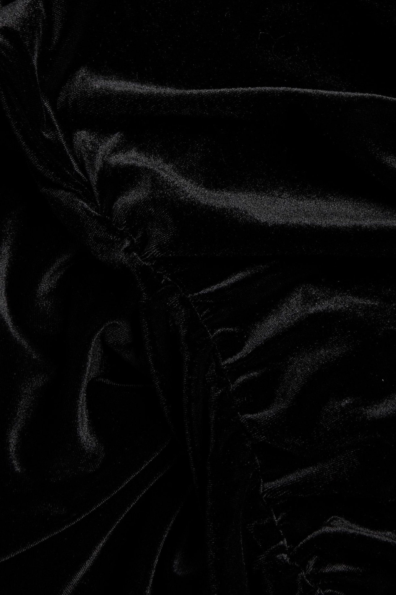 Zbliżenie czarnej aksamitnej tkaniny sukienkowej, ukazujące jej miękką fakturę, subtelny połysk i marszczenia.