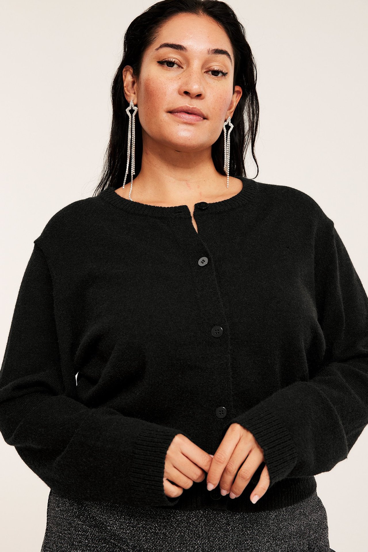 Edestä, nainen mustassa neulotussa neuletakissa, pitkät hopeakorvakorut ja kimalteleva tumma hame.