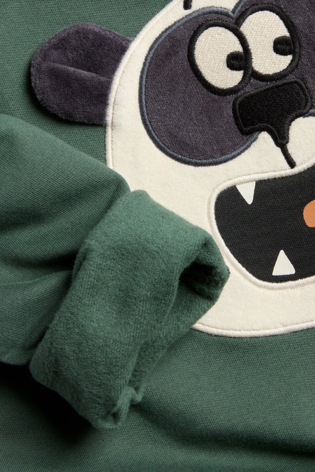 Zbliżenie zielonej bawełnianej bluzy z dużą aplikacją pandy i ciemnymi uszami 3D.