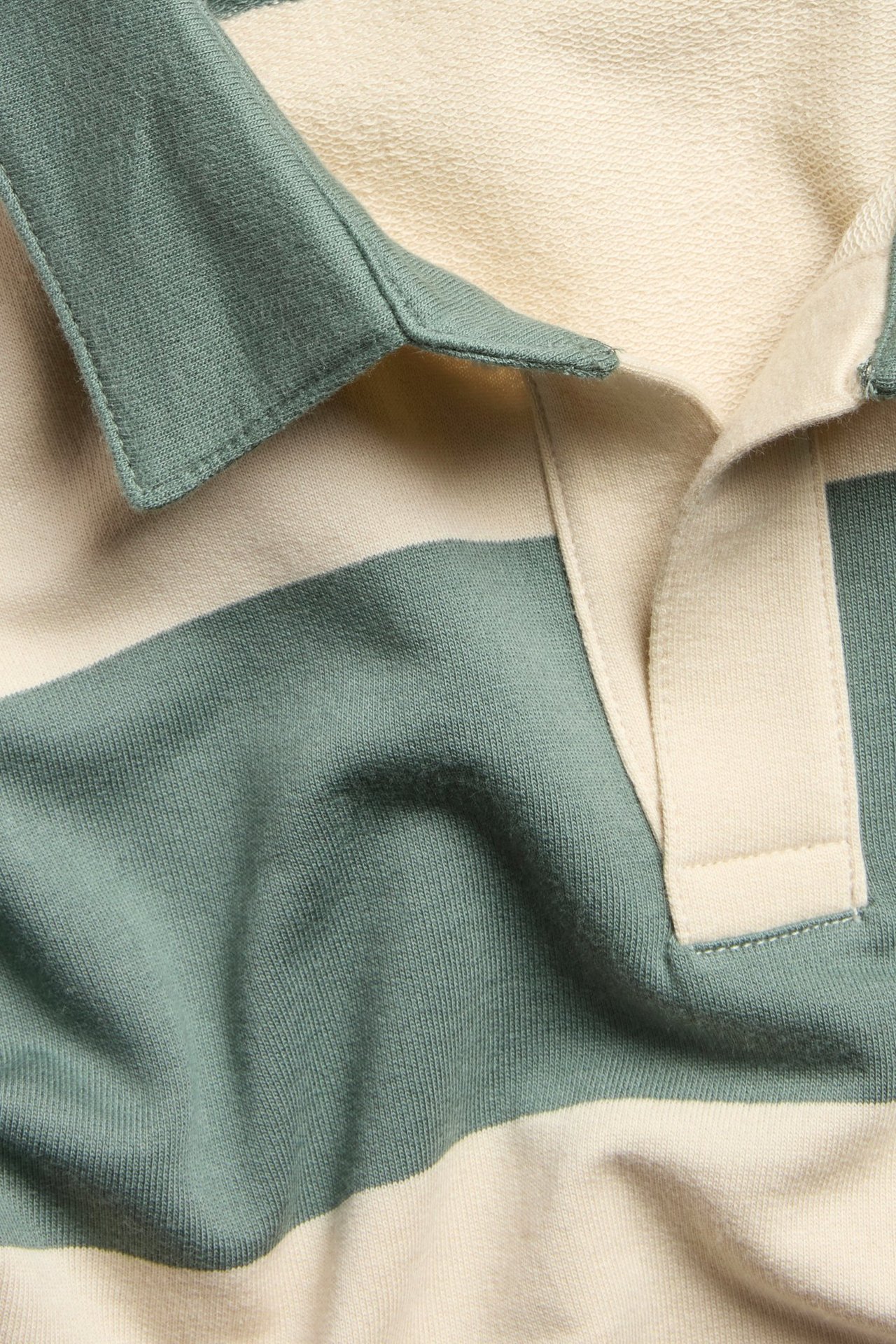 Zbliżenie na pasiastą bawełnianą bluzę polo w jasnym beżu i stonowanej zieleni z kołnierzykiem.
