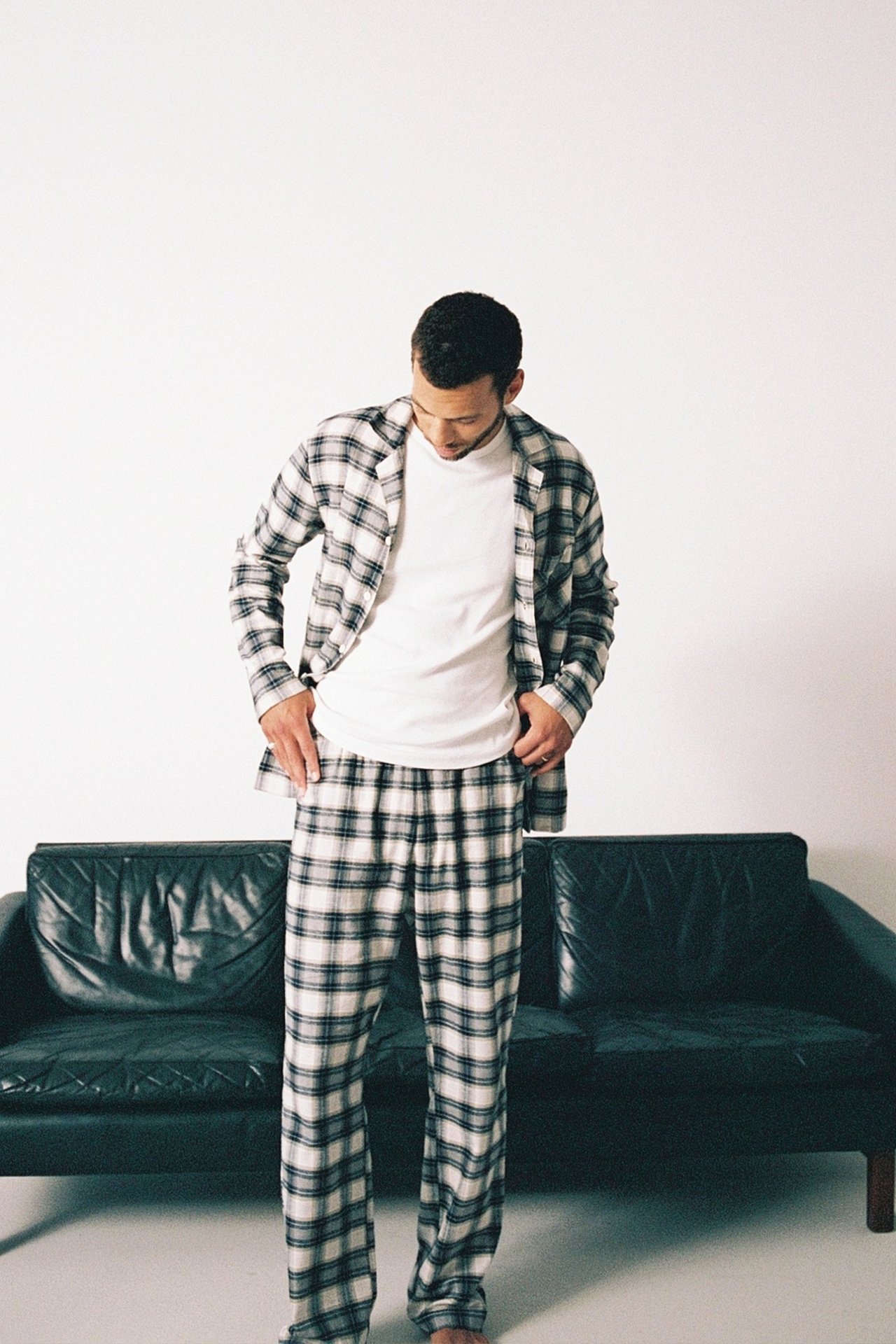 Mężczyzna w beżowym jaskrawo-kraciastym pidżamie, przed sofą.