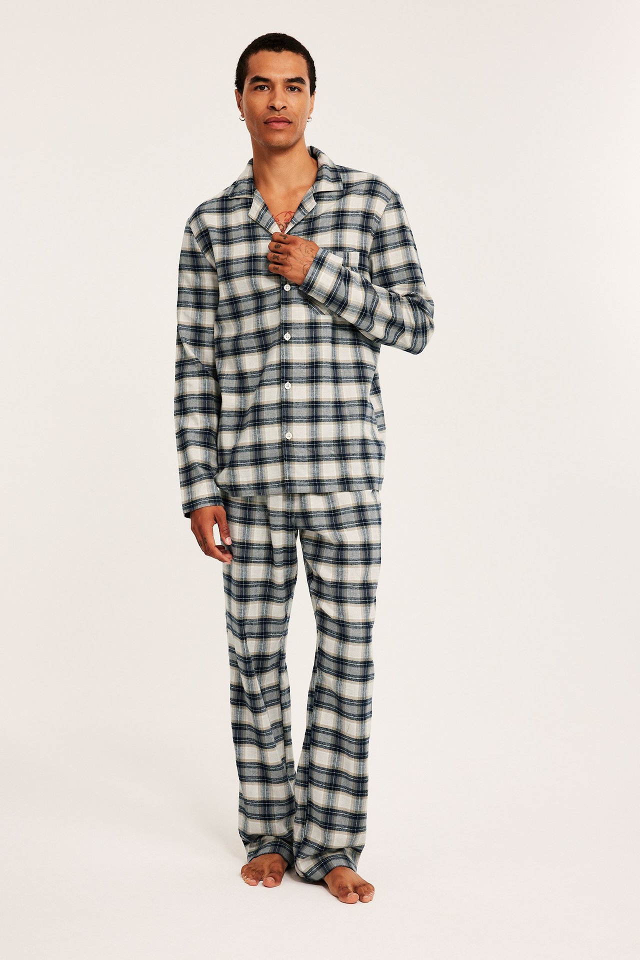 Frontvy av en man i en beige och mörkblå rutig flanellpyjamas med knäppt överdel och byxor.