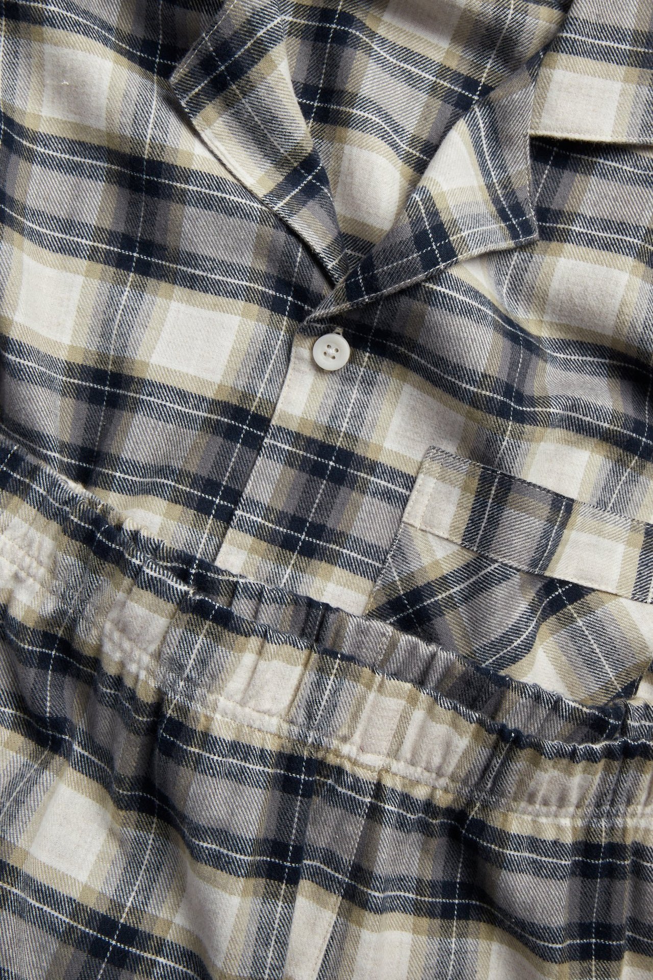 Zbliżenie męskiej beżowej piżamy z flaneli w kratę. Koszula z guzikami, kieszenią i pasujące spodnie z gumką.