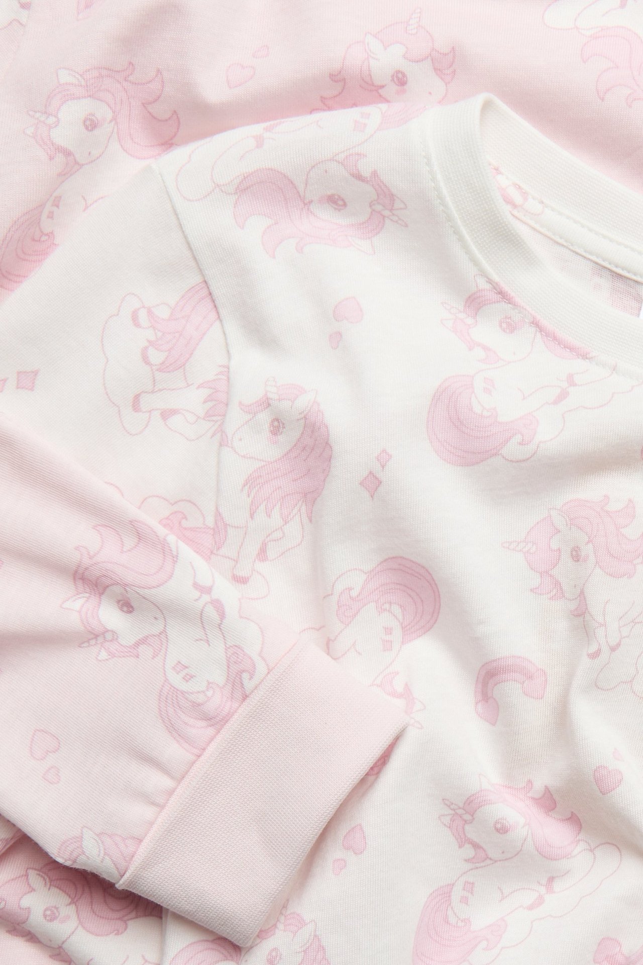 Zbliżenie na jasnoróżową bawełnianą piżamę dziecięcą z różowym wzorem jednorożca i ściągaczami.