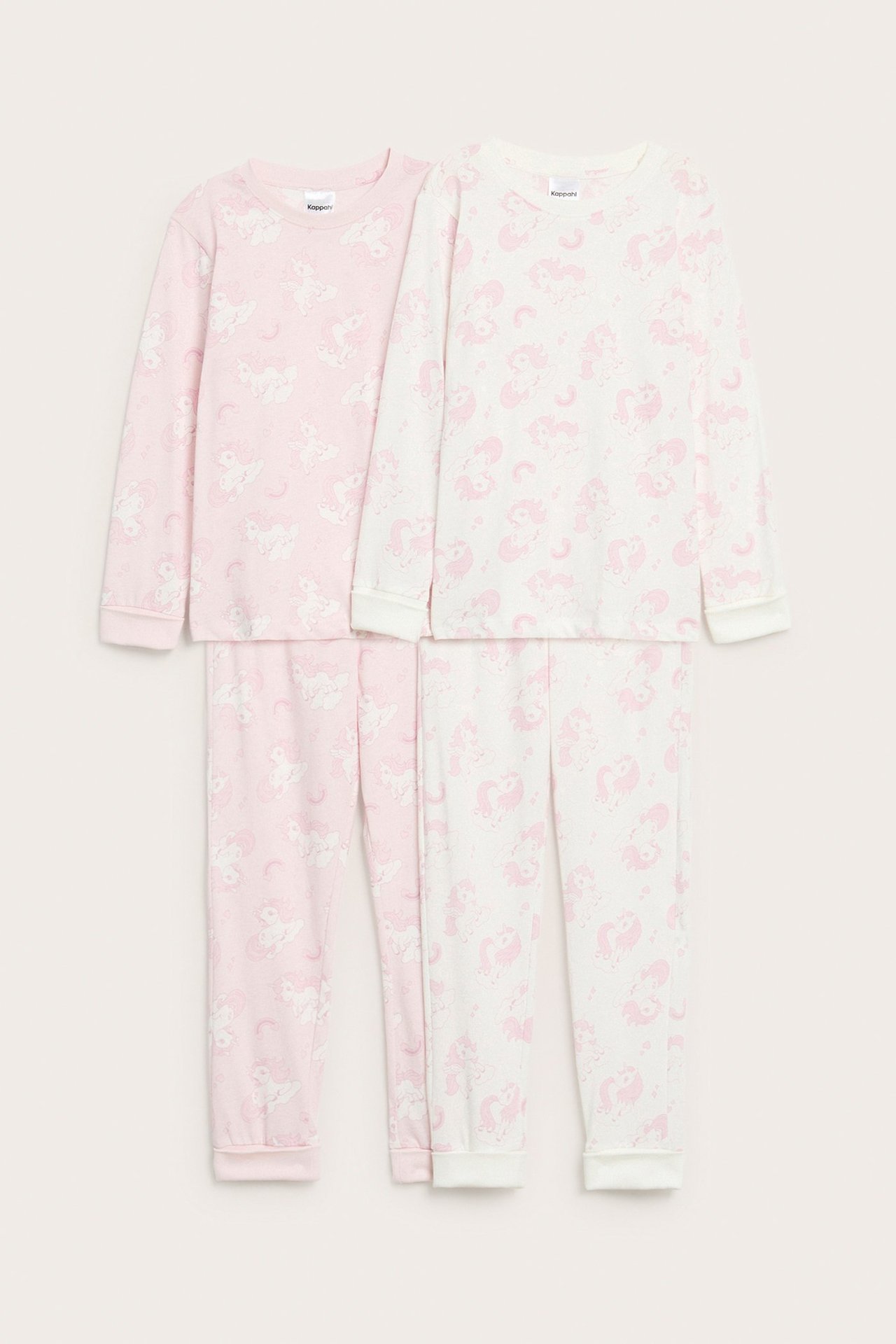 Edestä: kaksi lasten puuvillapyjamassettiä; vaaleanpunainen ja luonnonvalkoinen, molemmissa vaaleanpunainen yksisarviskuvio.