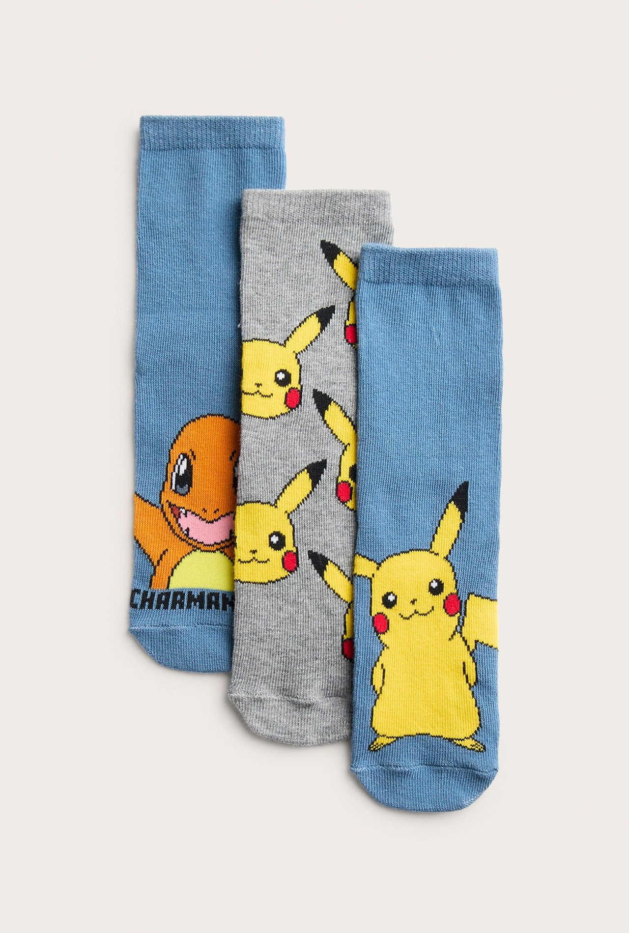 Edestä, 3 paria lasten sukkia: siniset Charmander-sukat, harmaat Pikachu-kasvot, ja siniset Pikachu-sukat.