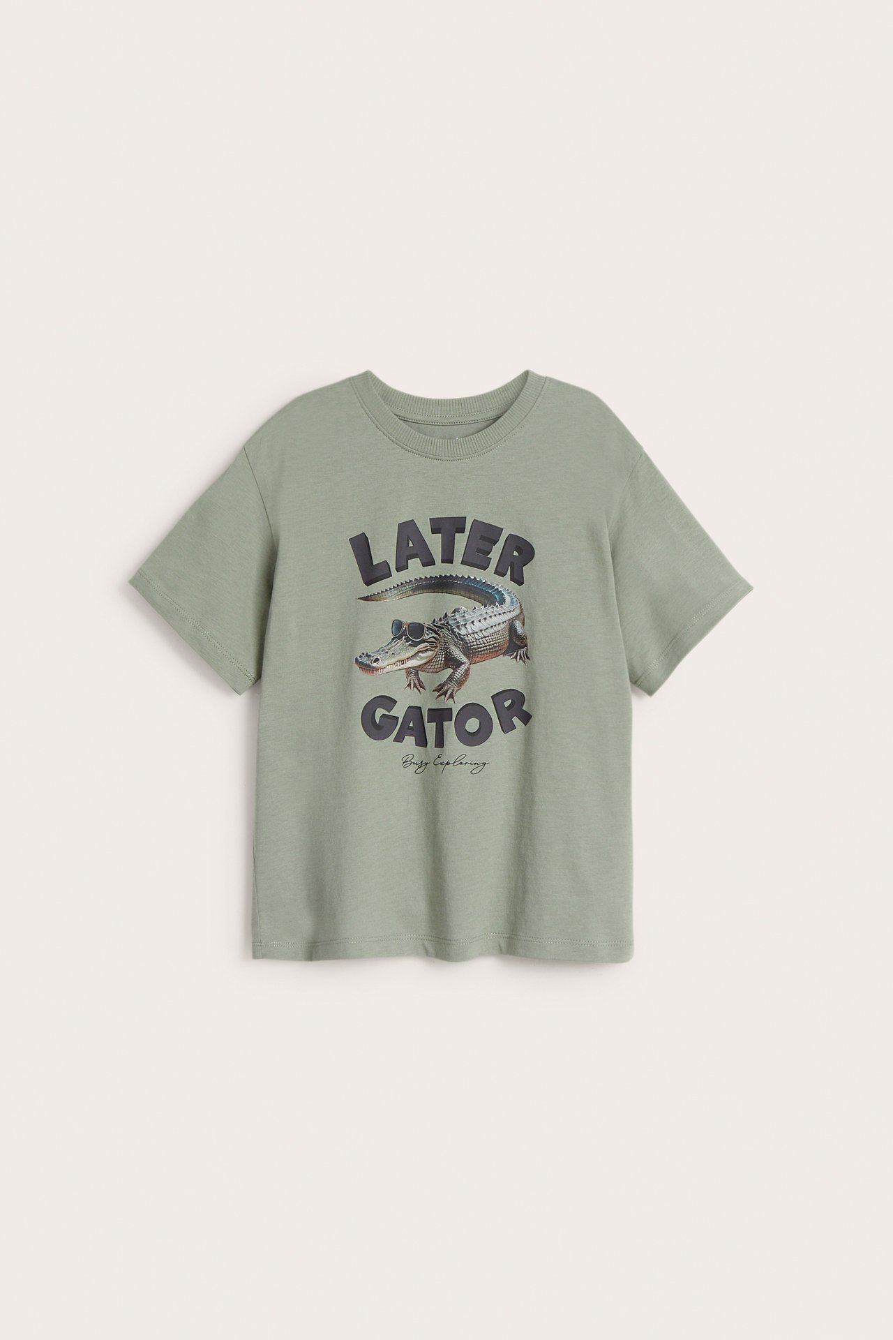 Forfra, en mørkegrønn t-skjorte i bomull for barn med et "Later Gator" alligator-trykk.