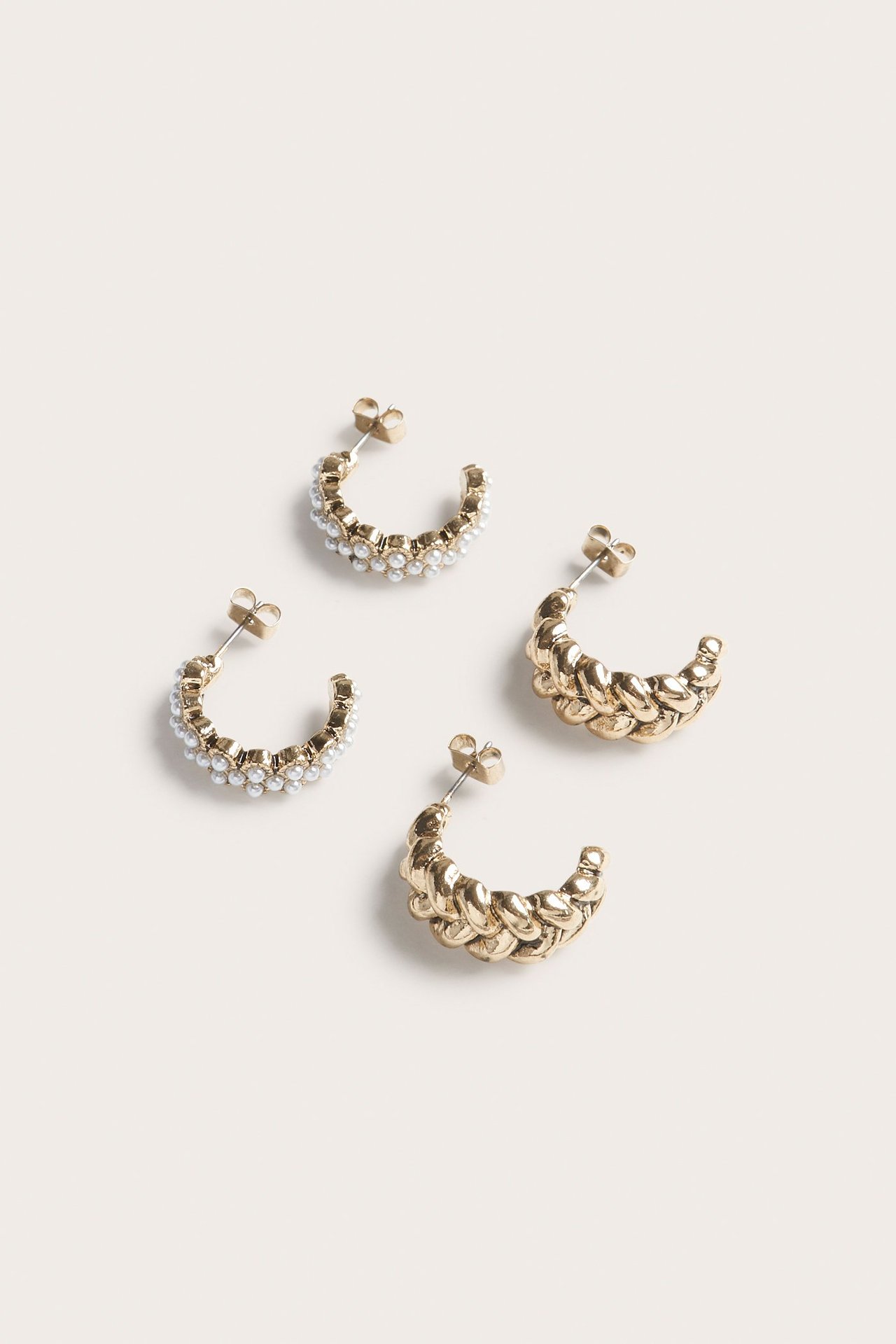 Widok z góry na dwie pary złotych kolczyków: jedne z małymi białymi perłami, drugie plecione.