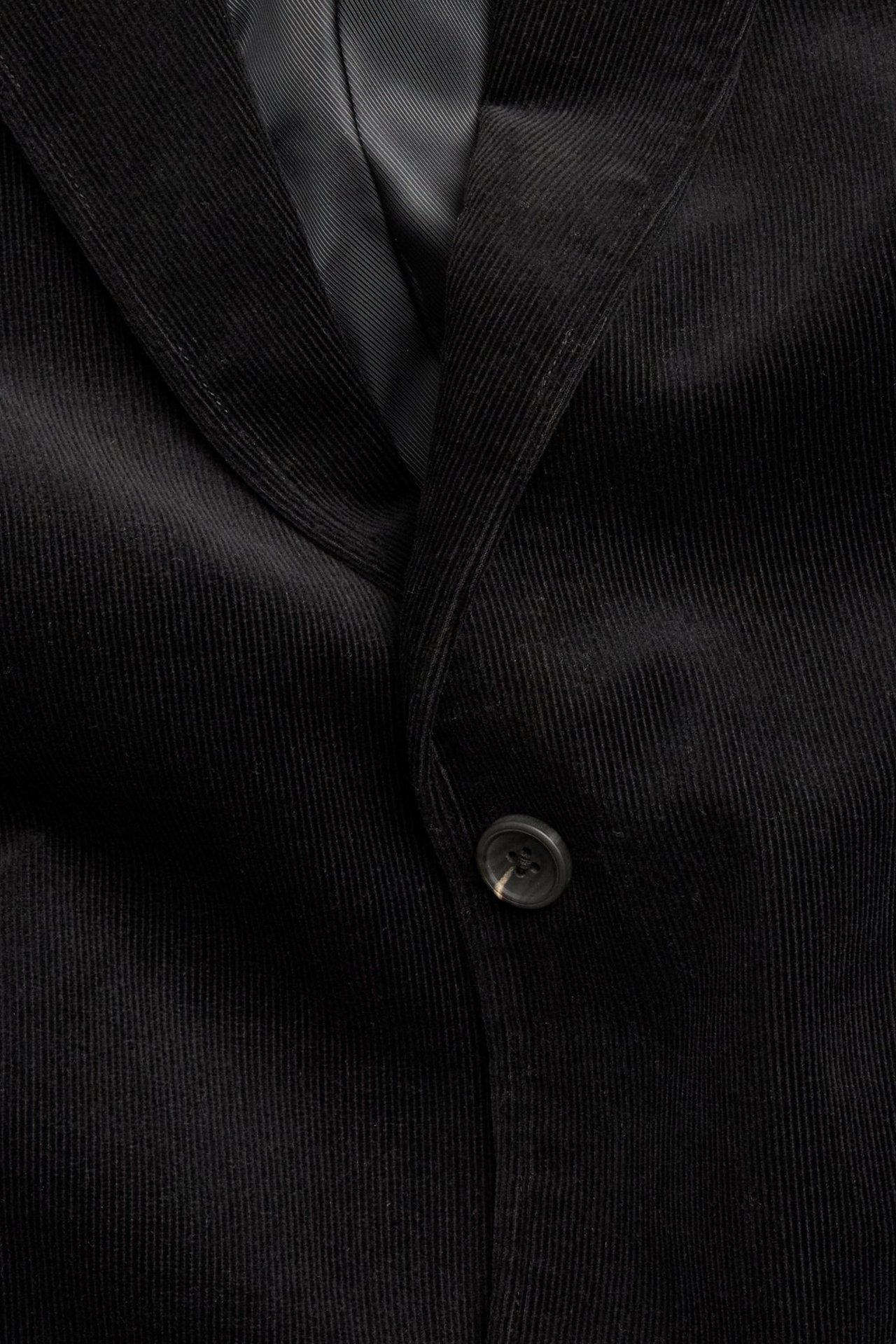 Zbliżenie czarnej jednorzędowej sztruksowej marynarki z jednym guzikiem.