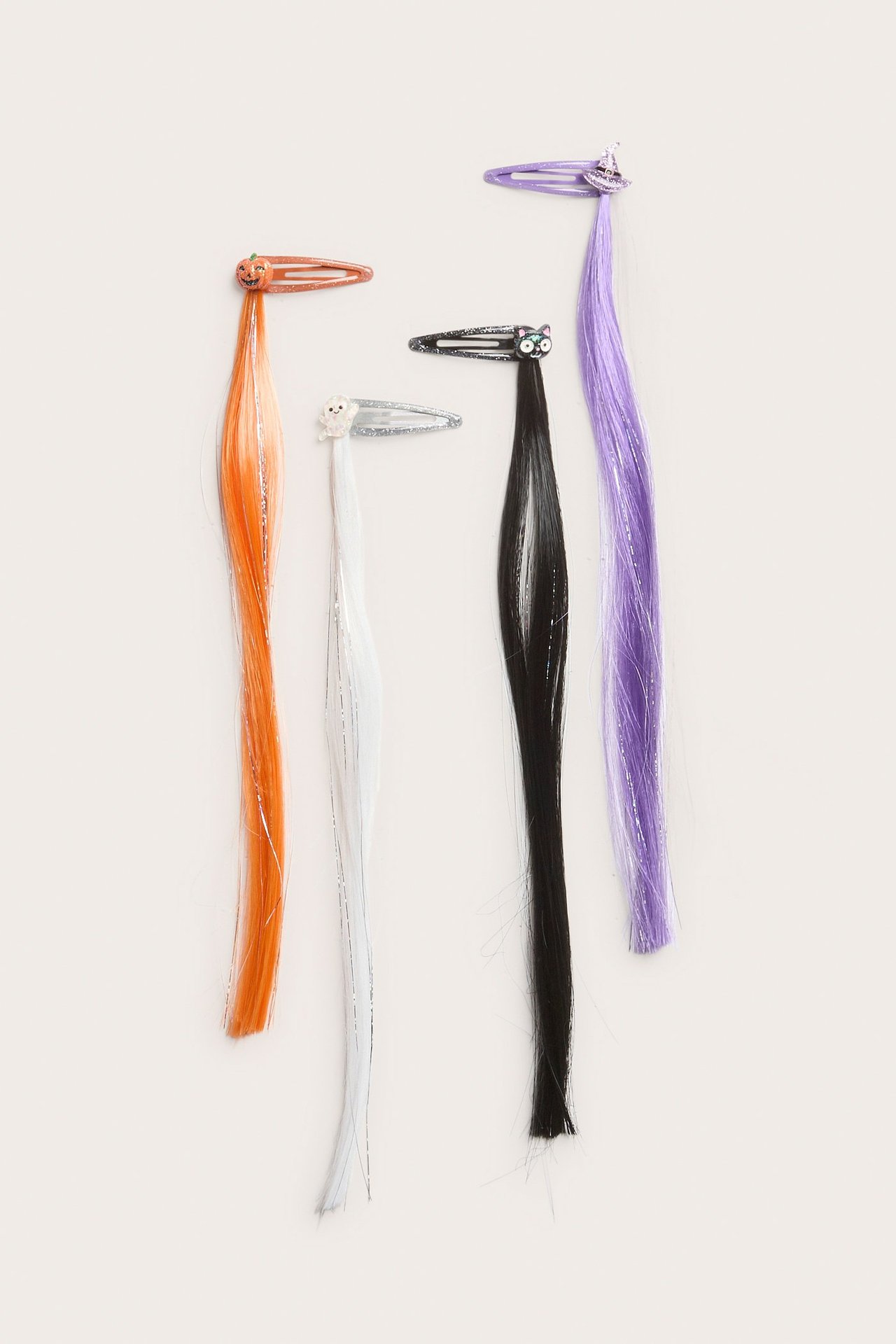 Ylhäältä näkymä neljästä kimaltavasta halloween-hiussoljesta tekohiuksilla oranssina, valkoisena, mustana ja violettina.