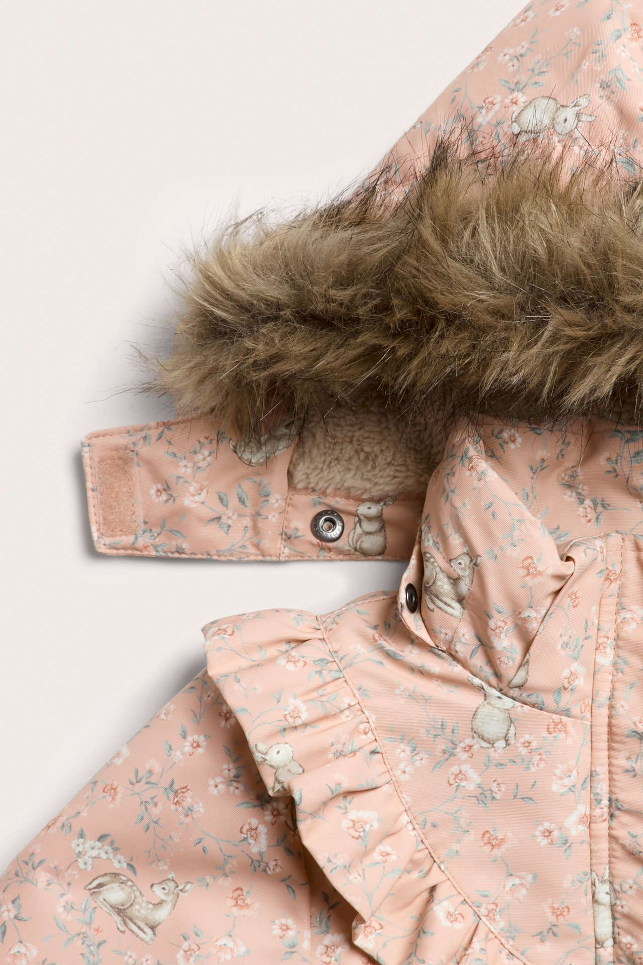 Lähikuva vaaleanpunaisesta topatusta lastentakista, jossa kukka- ja eläinkuvio, tekoturkishuppu, rypytykset ja nepparit.