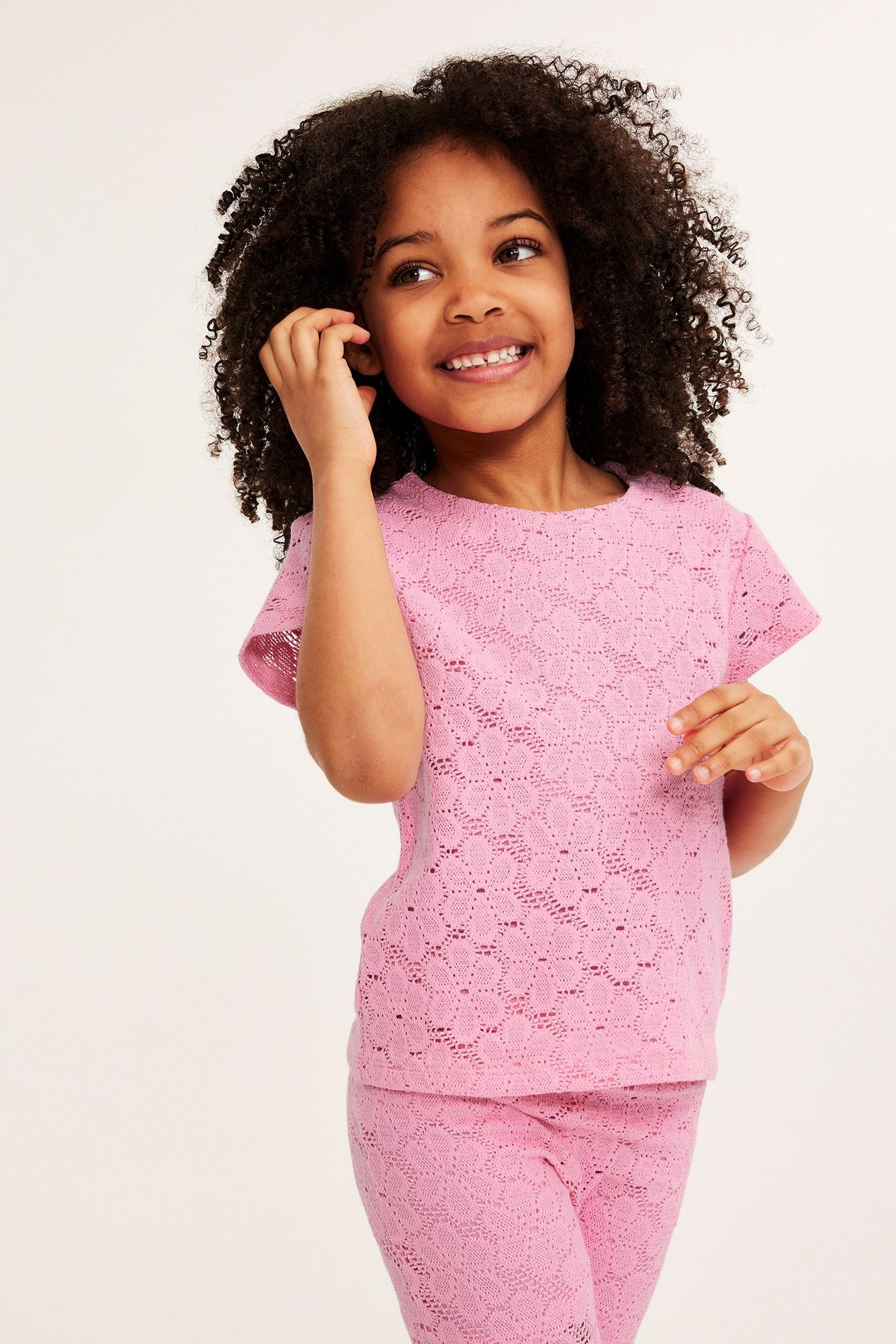 Widok z przodu dziecka w różowym koronkowym topie z krótkim rękawem i pasujących koronkowych legginsach.