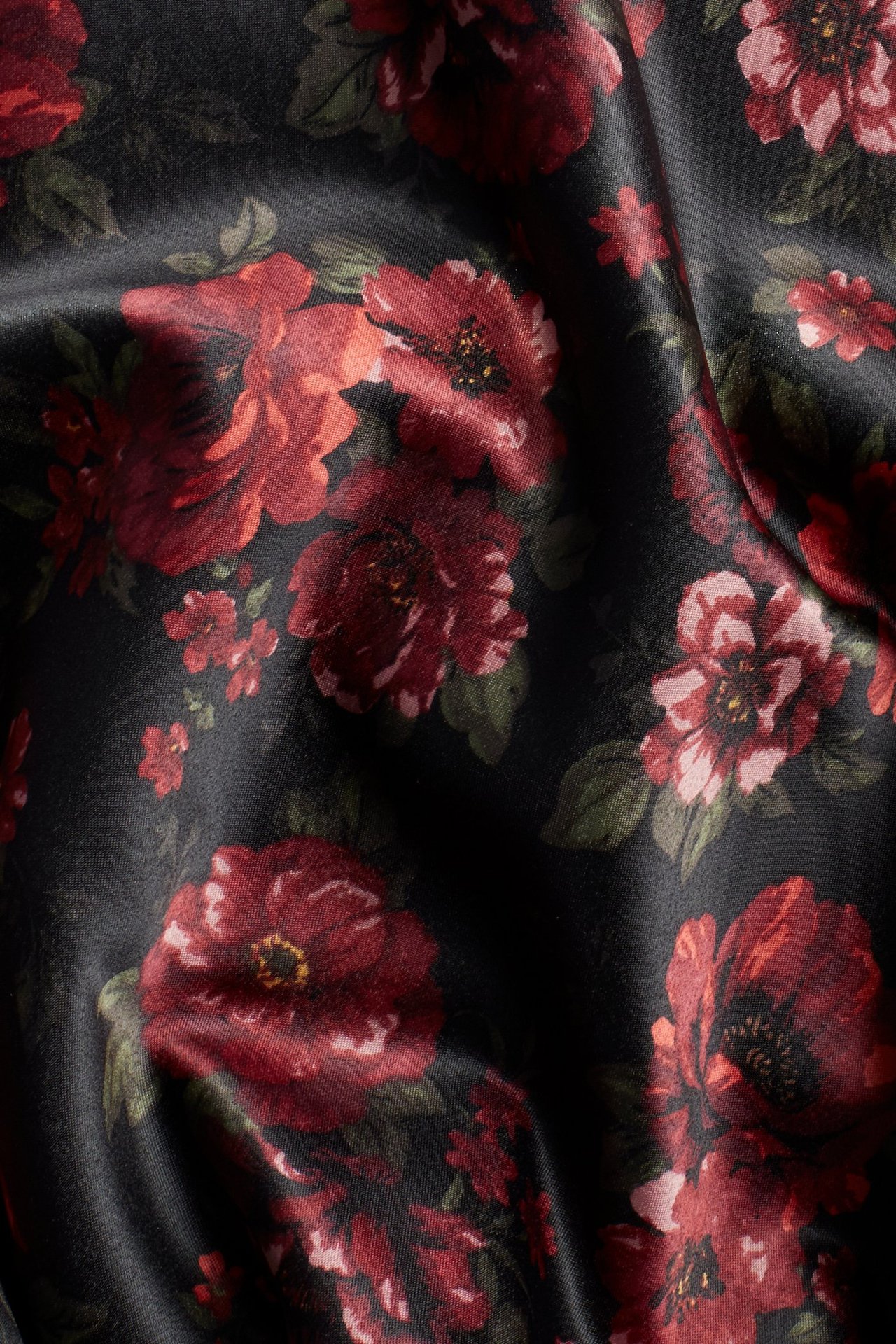 Zbliżenie czarnej spódnicy z tafty z ciemnoczerwonym kwiatowym wzorem.