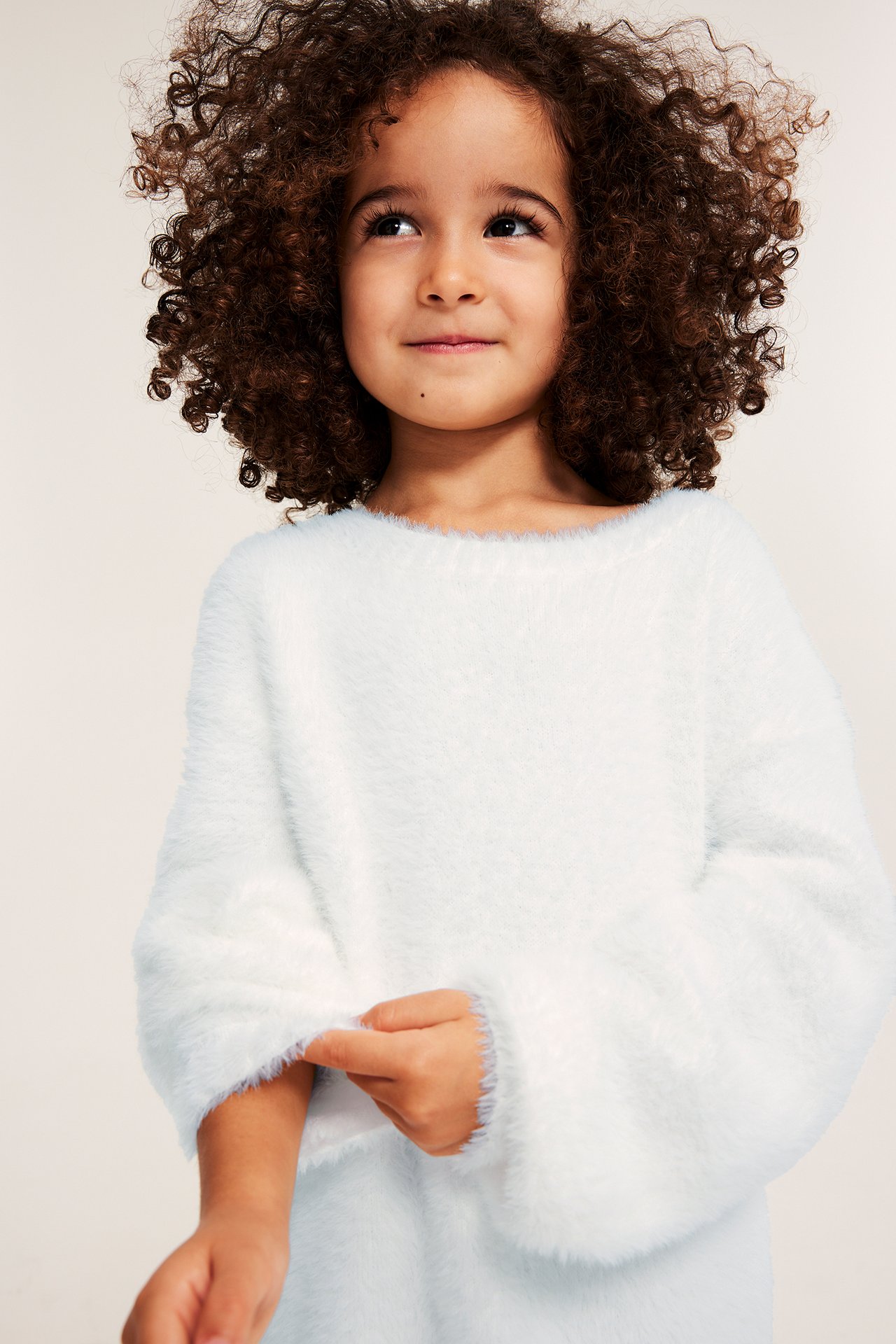 Forsiden: Et barn i en offwhite, luftig strikkegenser i feather yarn med rund hals.
