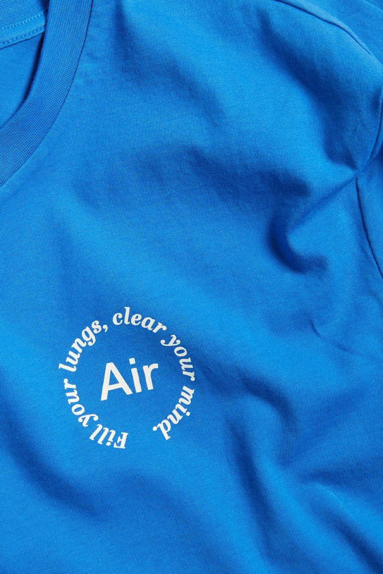 Zbliżenie z przodu na niebieską bawełnianą koszulkę z białym okrągłym nadrukiem 'Air'.