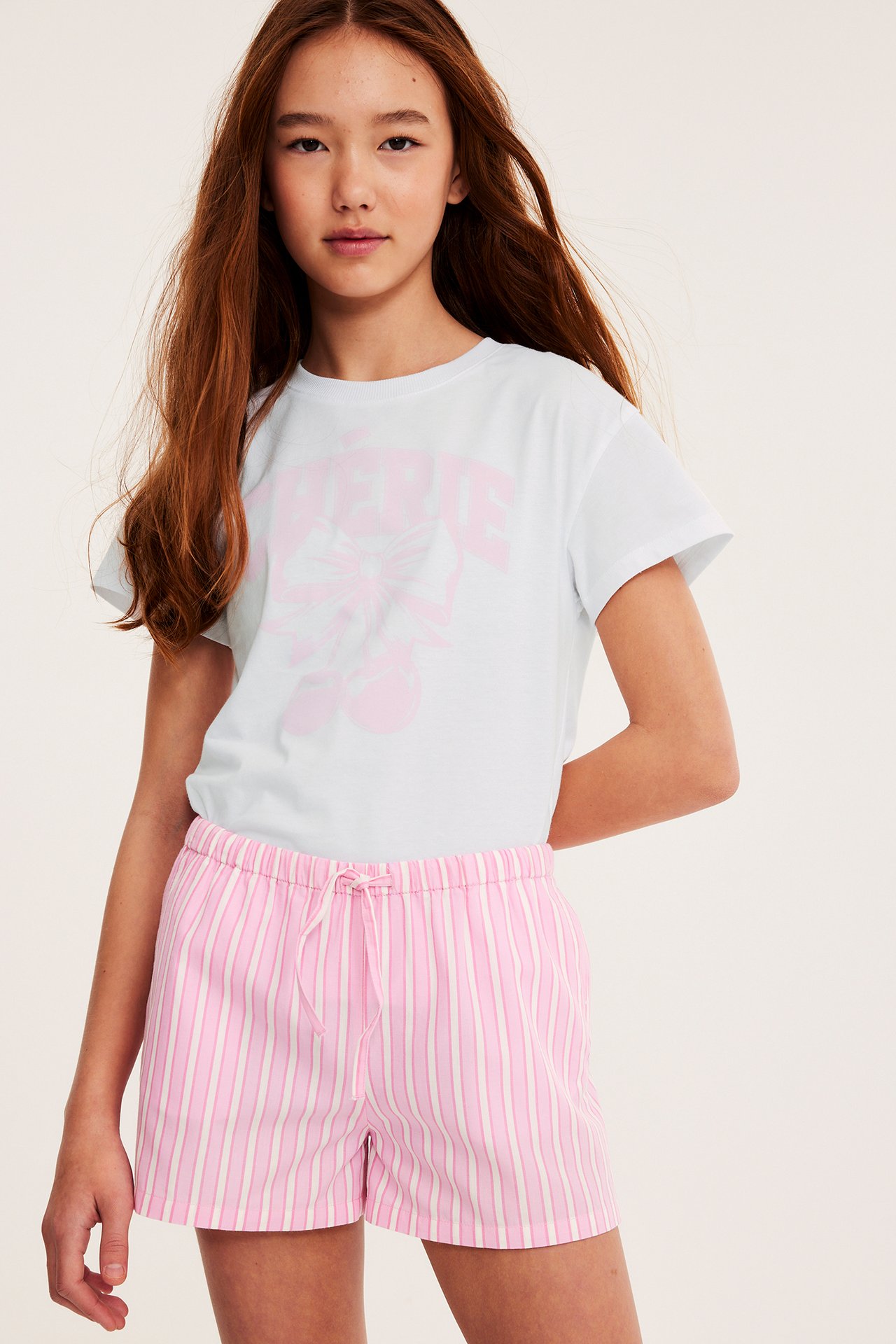 Biały T-shirt z nadrukiem z przodu i małym serduszkiem na karku, młoda kobieta