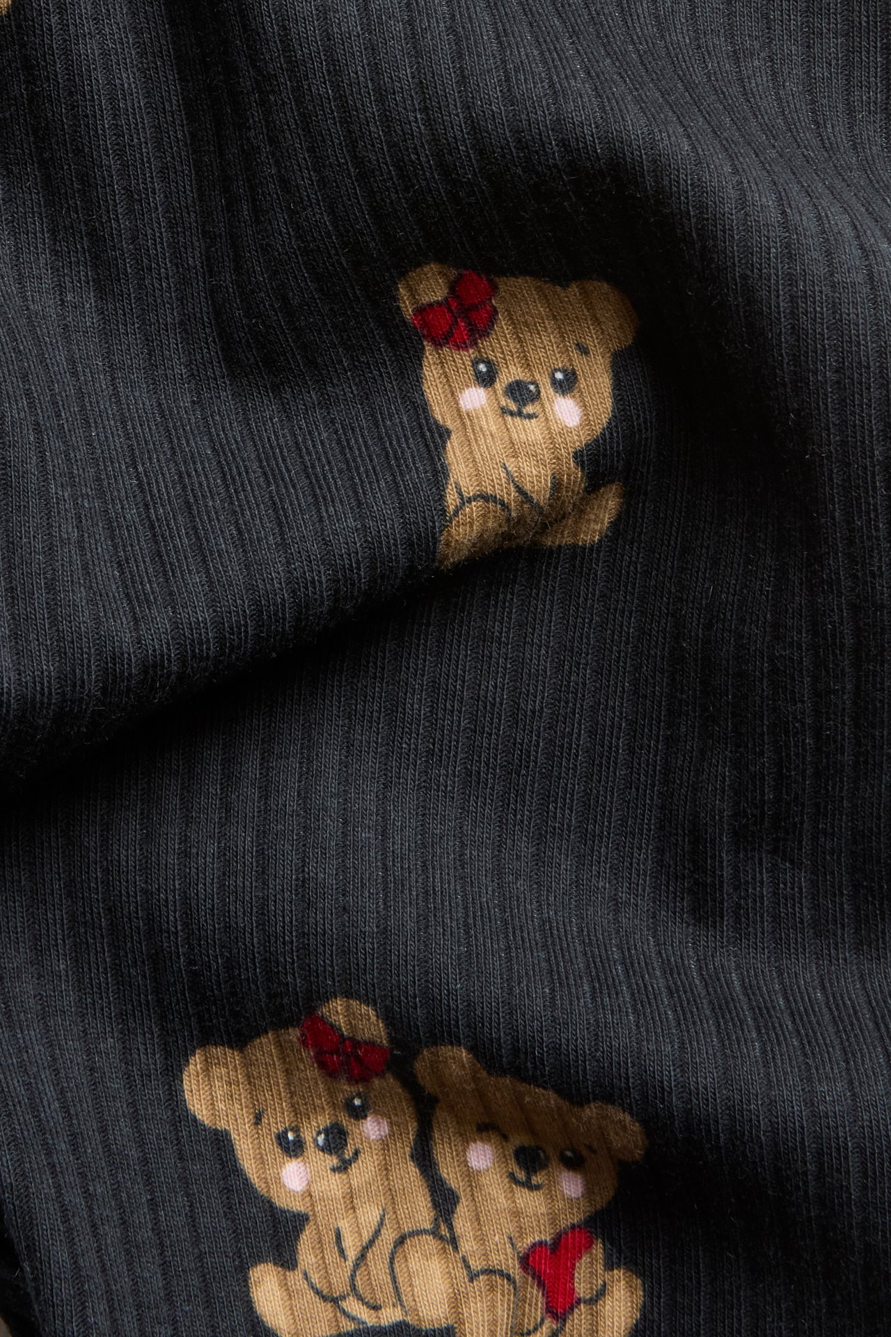 Nærbilde av svarte ribbestrikkede leggings med brunt teddybjørnmønster.