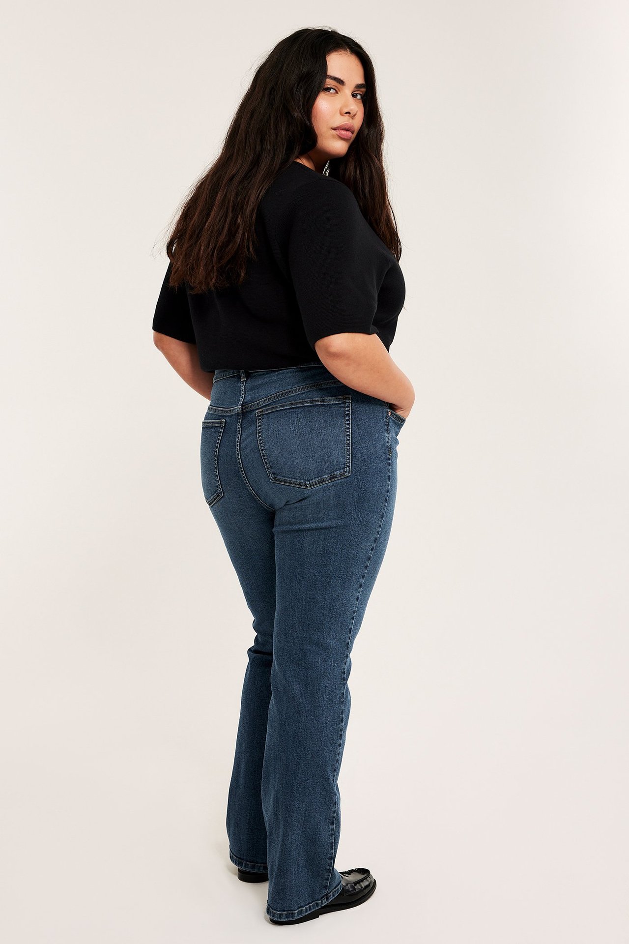 Z boku i z tyłu: kobieta w niebieskich dżinsach bootcut z wysokim stanem, czarnym topie i mokasynach.