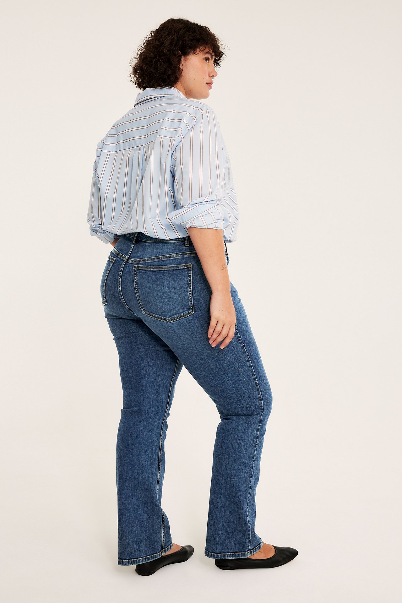 Sidovy av kvinna i blå utsvängda jeans och ljusblå randig skjorta.