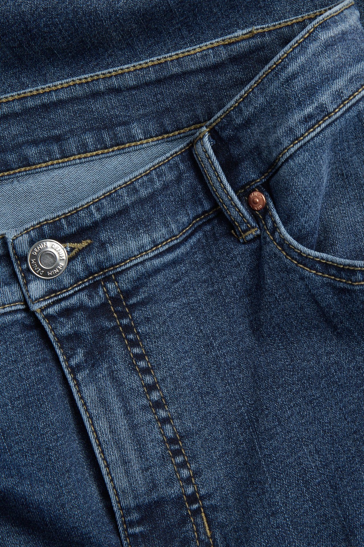 Nærbilde av mørkeblå high-waist bootcut jeans i denim med sølvknapp og sømmer.