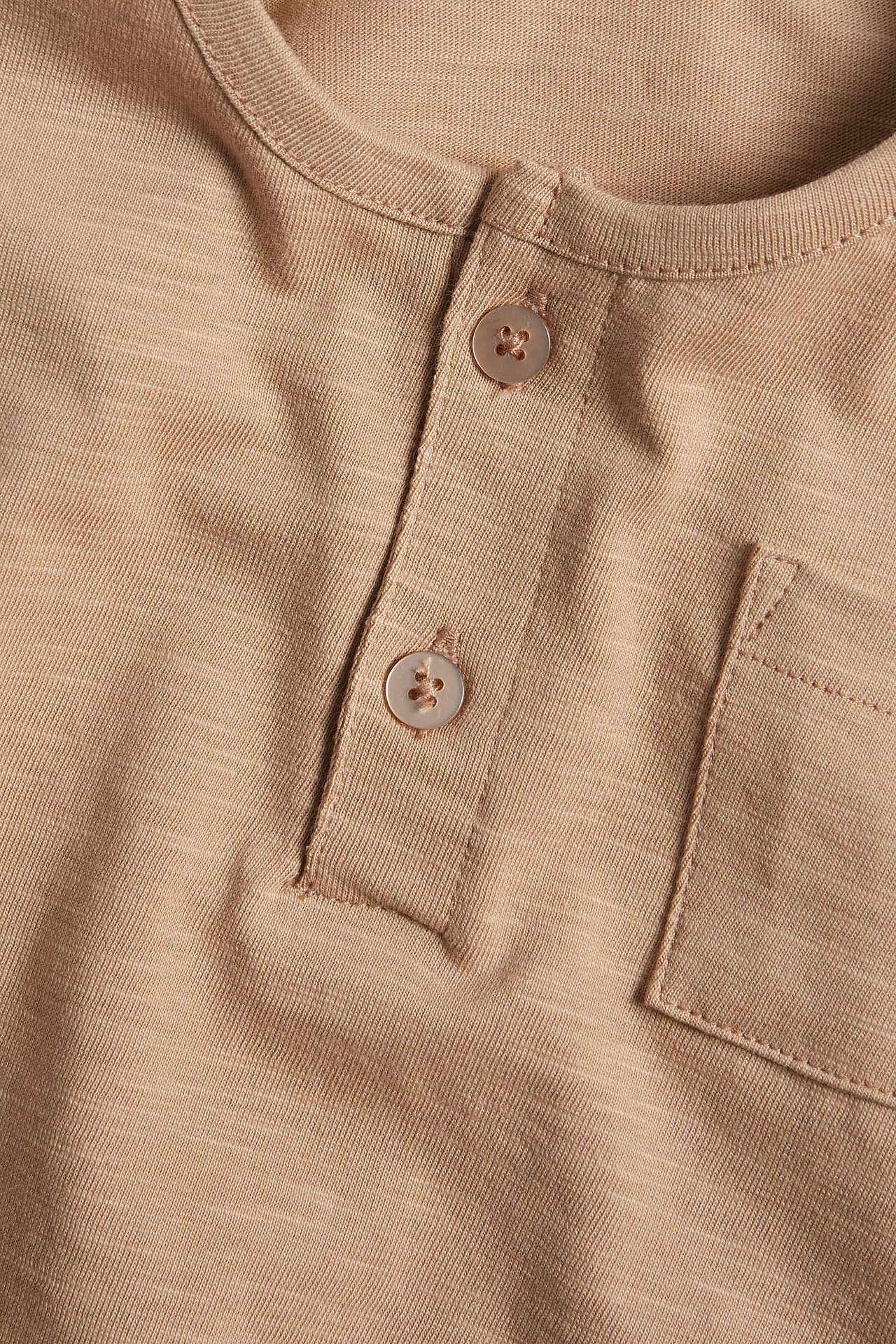 Zbliżenie brązowej koszulki z długim rękawem z dżerseju slub, z guzikami i kieszenią na piersi.