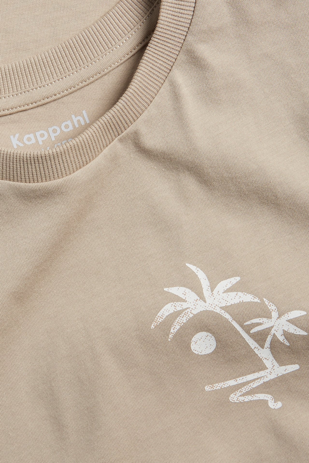 Närbild framifrån på en beige bomulls-t-shirt med vitt palmträdsmönster.