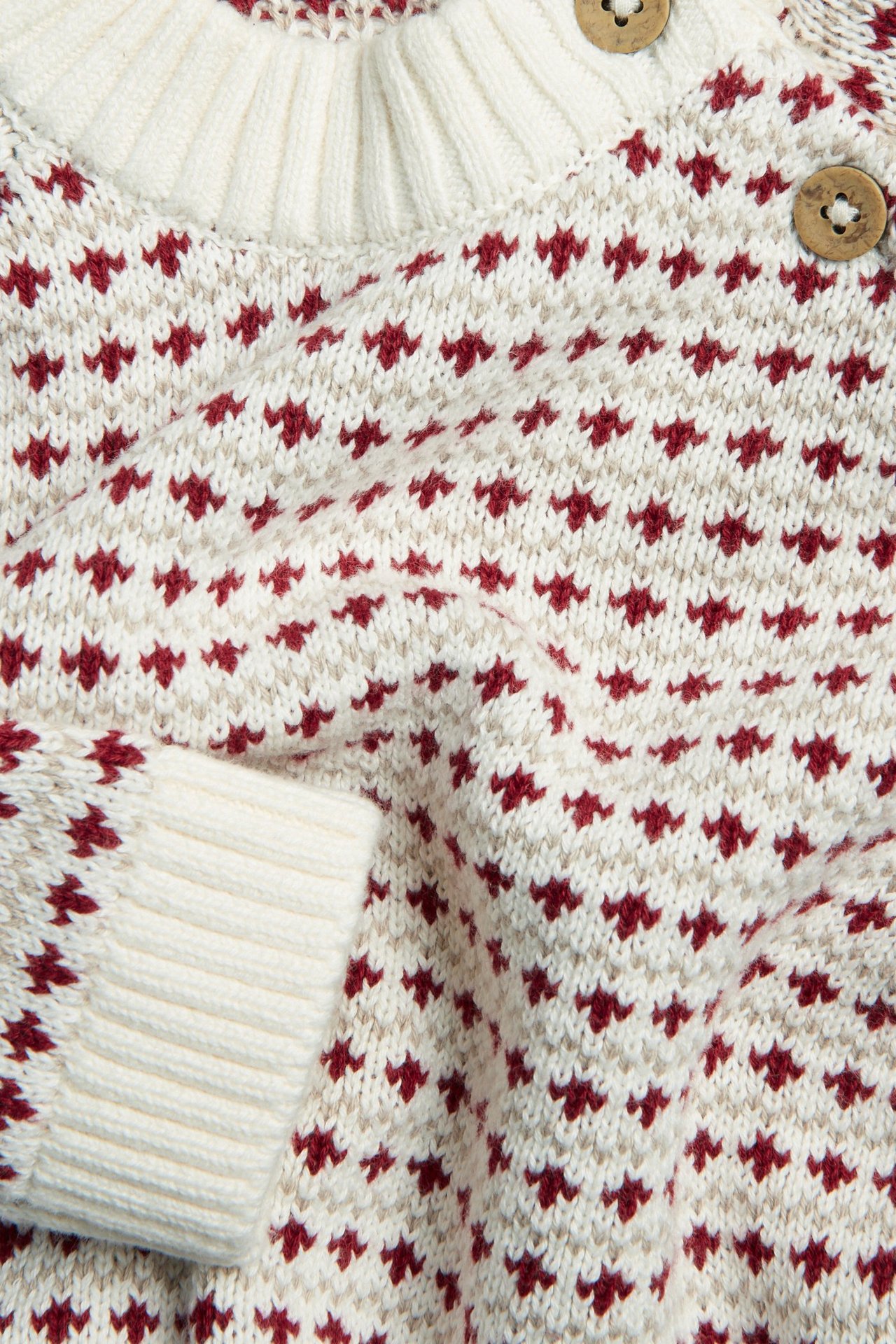 Lähikuva luonnonvalkoisesta neulepaidasta, jossa punainen ja beige jacquard-kuvio, resorihansuut ja puunapit.