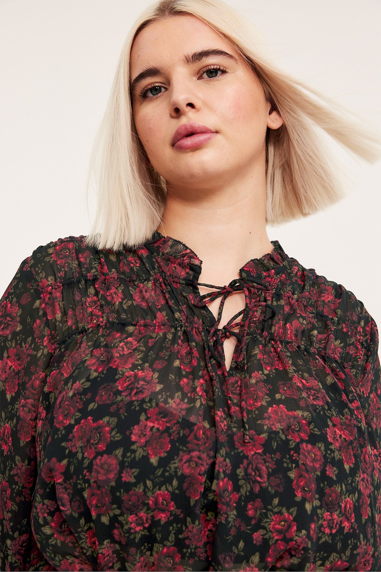 Framifrån på kvinna i svart långärmad blus med rött blommönster och snörning i halsen.