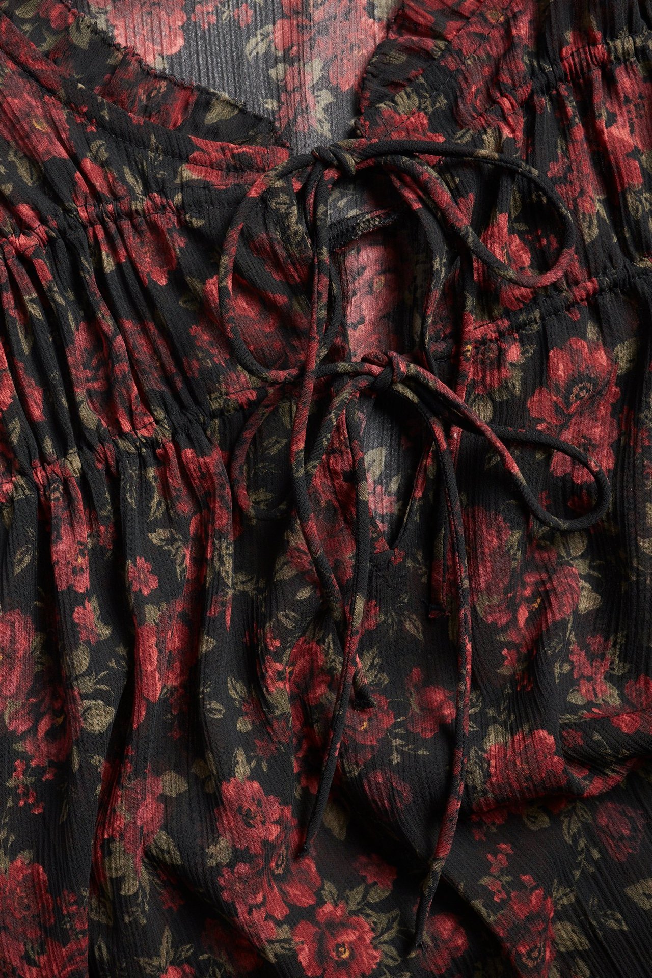 Zbliżenie czarnej wzorzystej bluzki poliestrowej z czerwonymi różami i dekoltem w serek ze sznurkiem.