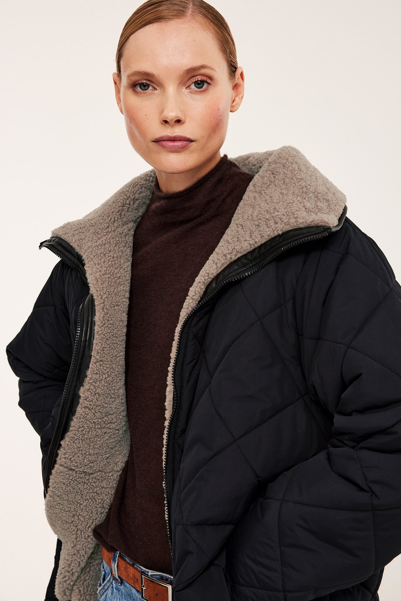 Framifrån: kvinna i svart quiltad jacka med brunt pilefoder över mörkbrun polotröja.
