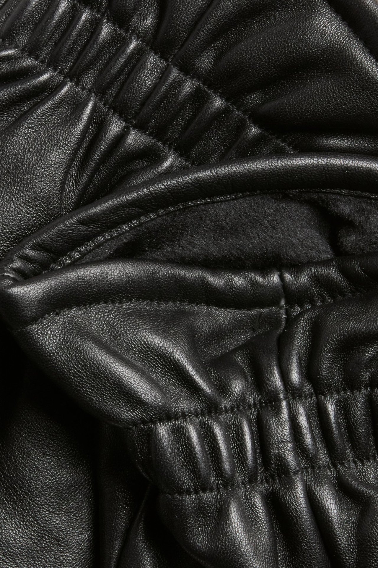 Zbliżenie czarnej skórzanej rękawiczki z pikowanymi szwami i widoczną poliestrową podszewką.