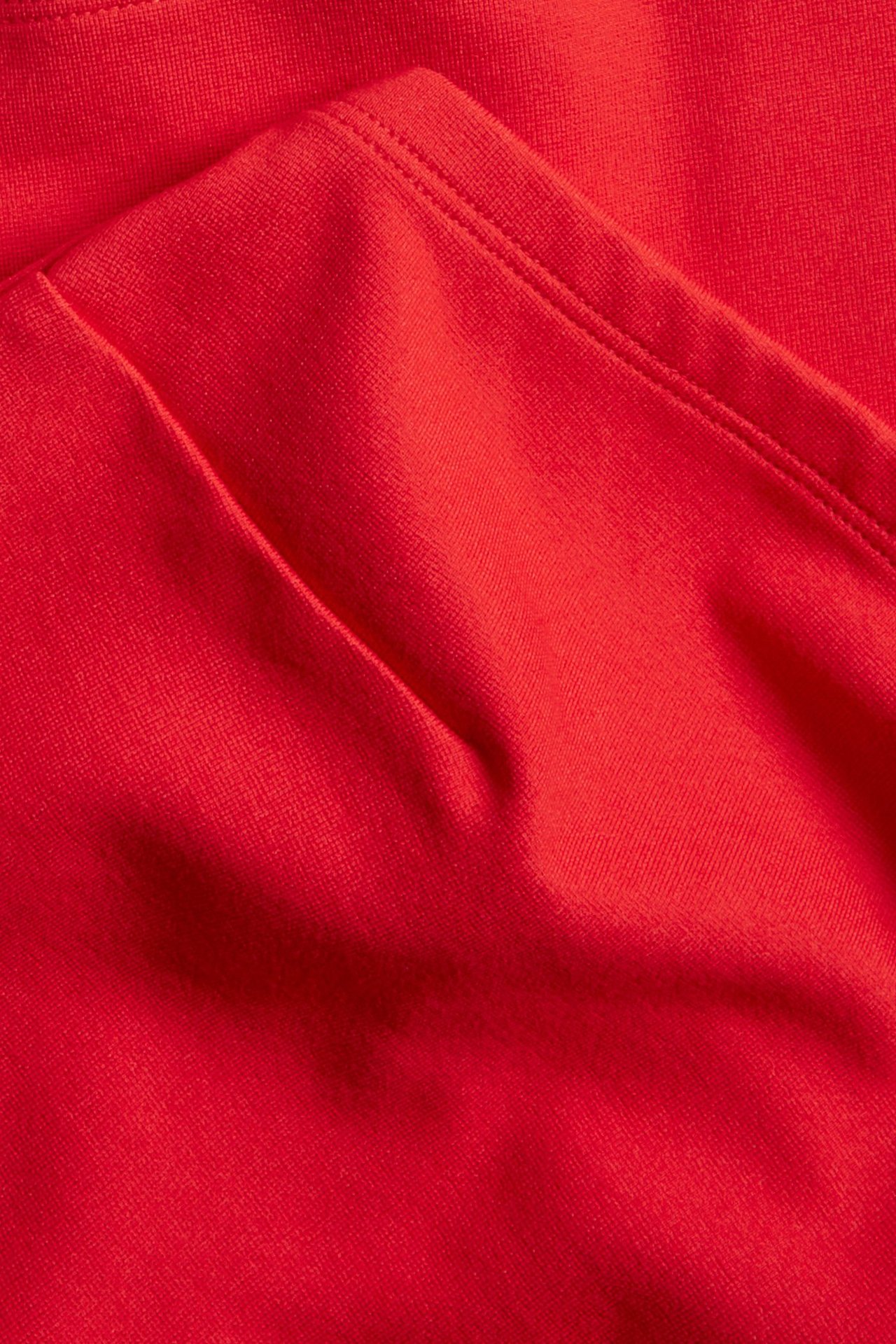 Zbliżenie na czerwony, dłuższy top tubowy z elastycznego materiału, pokazujące fałdy i szwy.