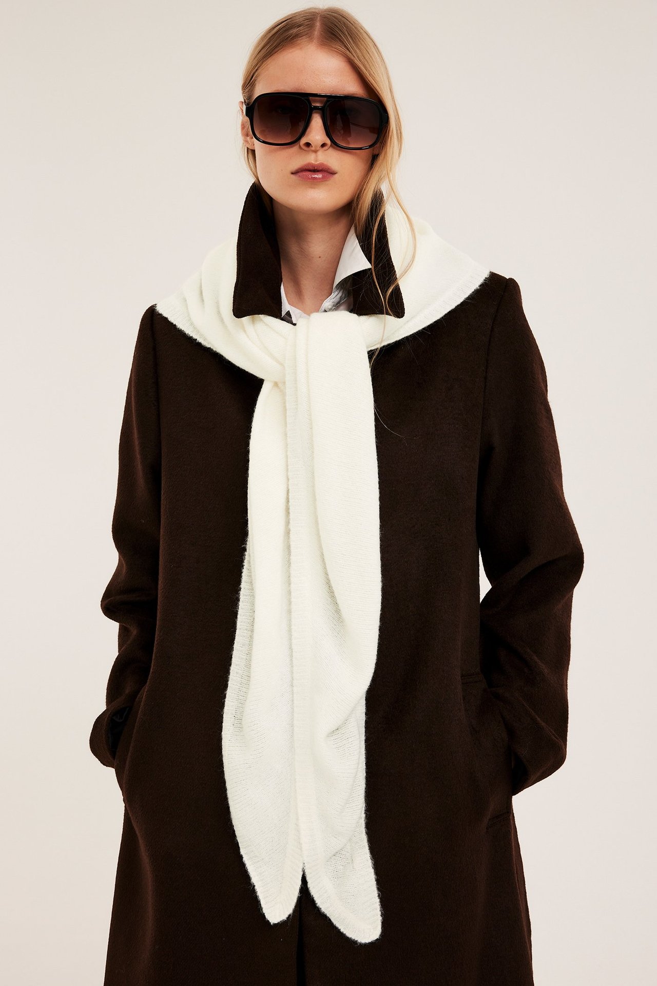 Kobieta z przodu: Ecru jednolity szalik trójkątny noszony na białej koszuli, ciemnobrązowym płaszczu i okularach.