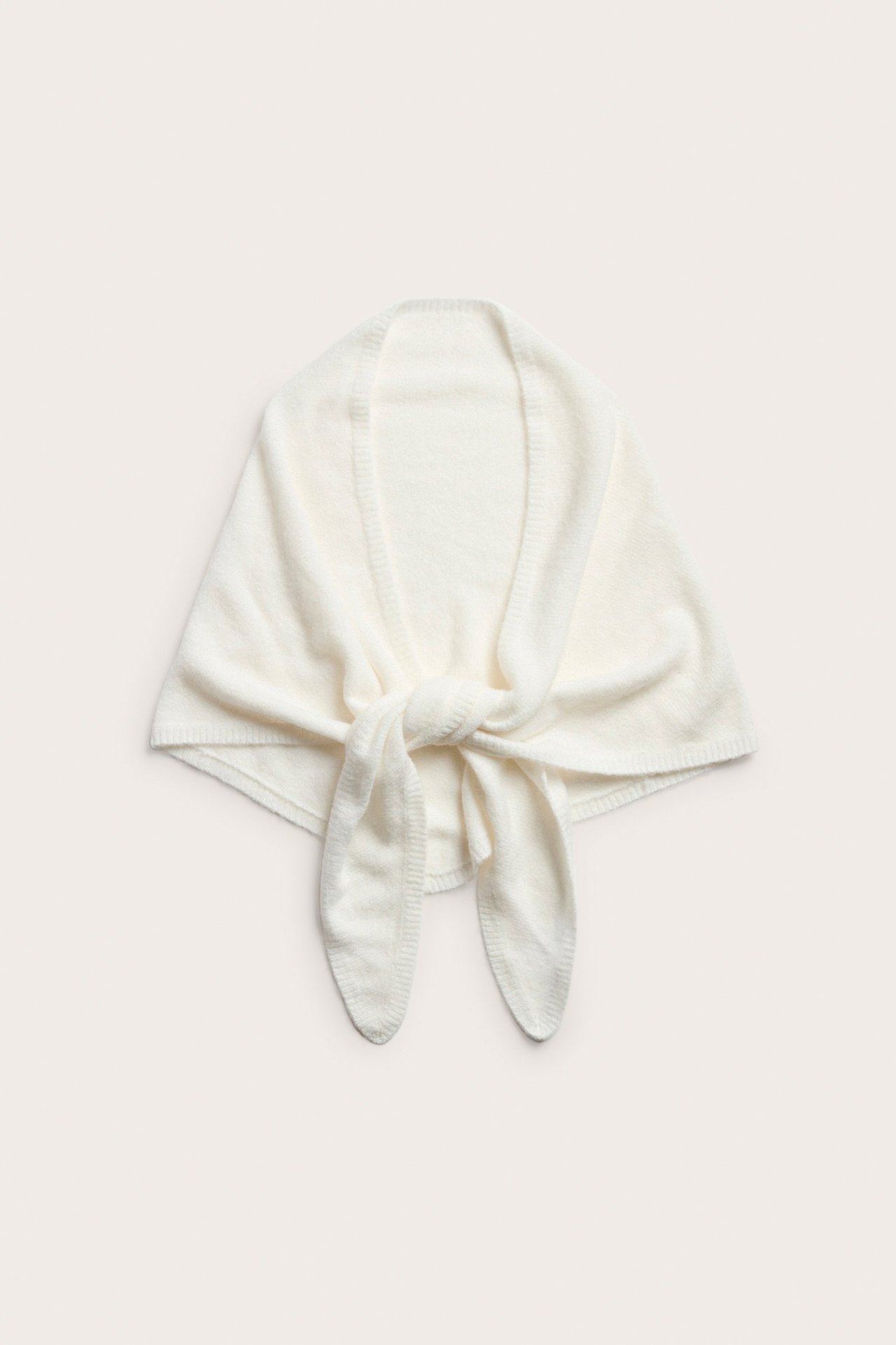 Widok z przodu kremowego dzianinowego szalika trójkątnego, zawiązanego z przodu.