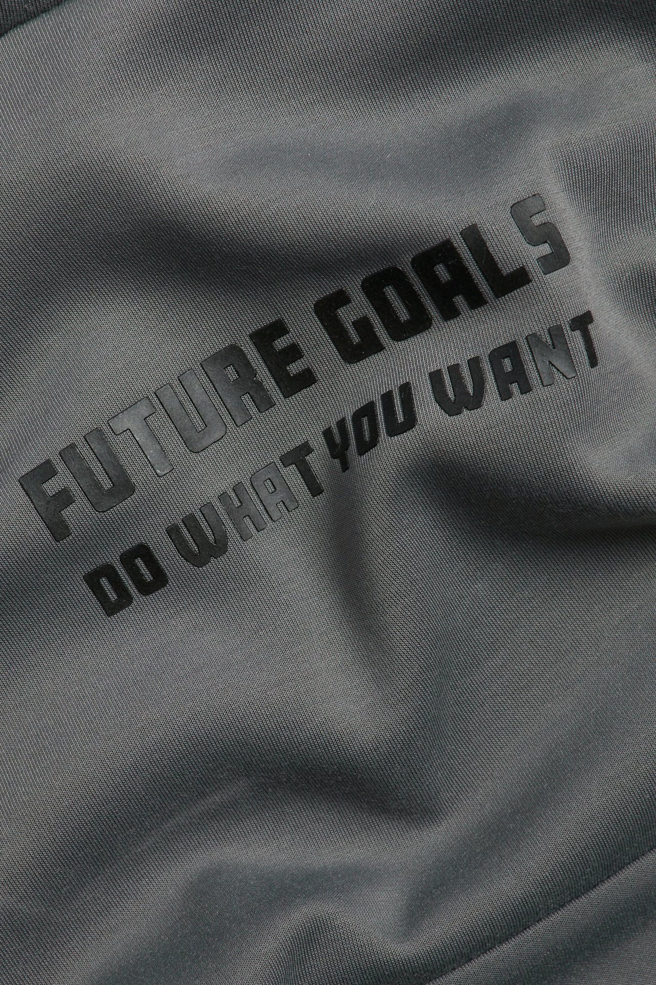 Zbliżenie na szary interlockowy materiał bluzy z wypukłym 3D nadrukiem: "FUTURE GOALS DO WHAT YOU WANT".