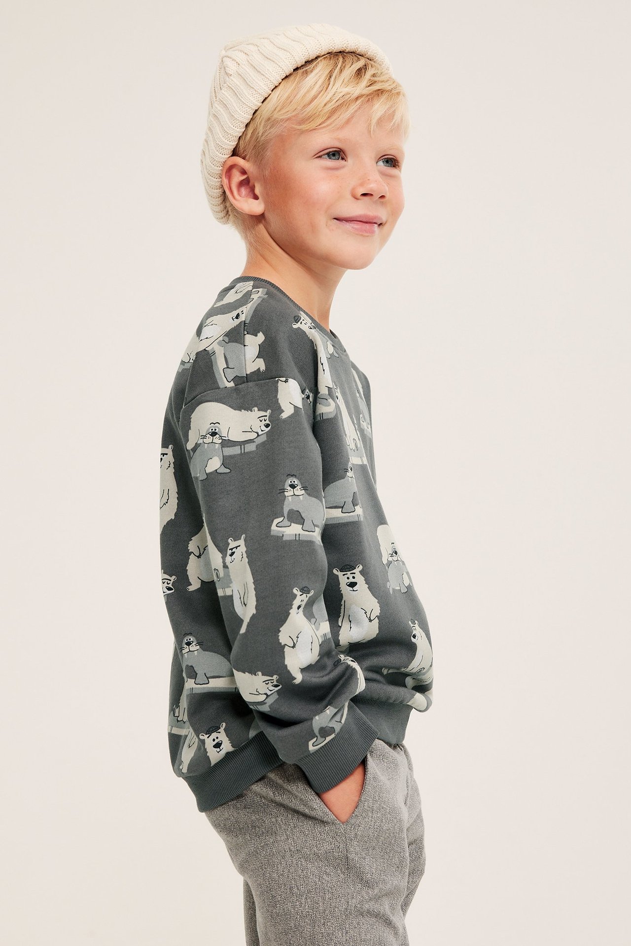 Sivukuva: Lapsi harmaassa puuvillapaidassa, jossa jääkarhukuvio, beigessä pipossa ja harmaissa collegehousuissa.