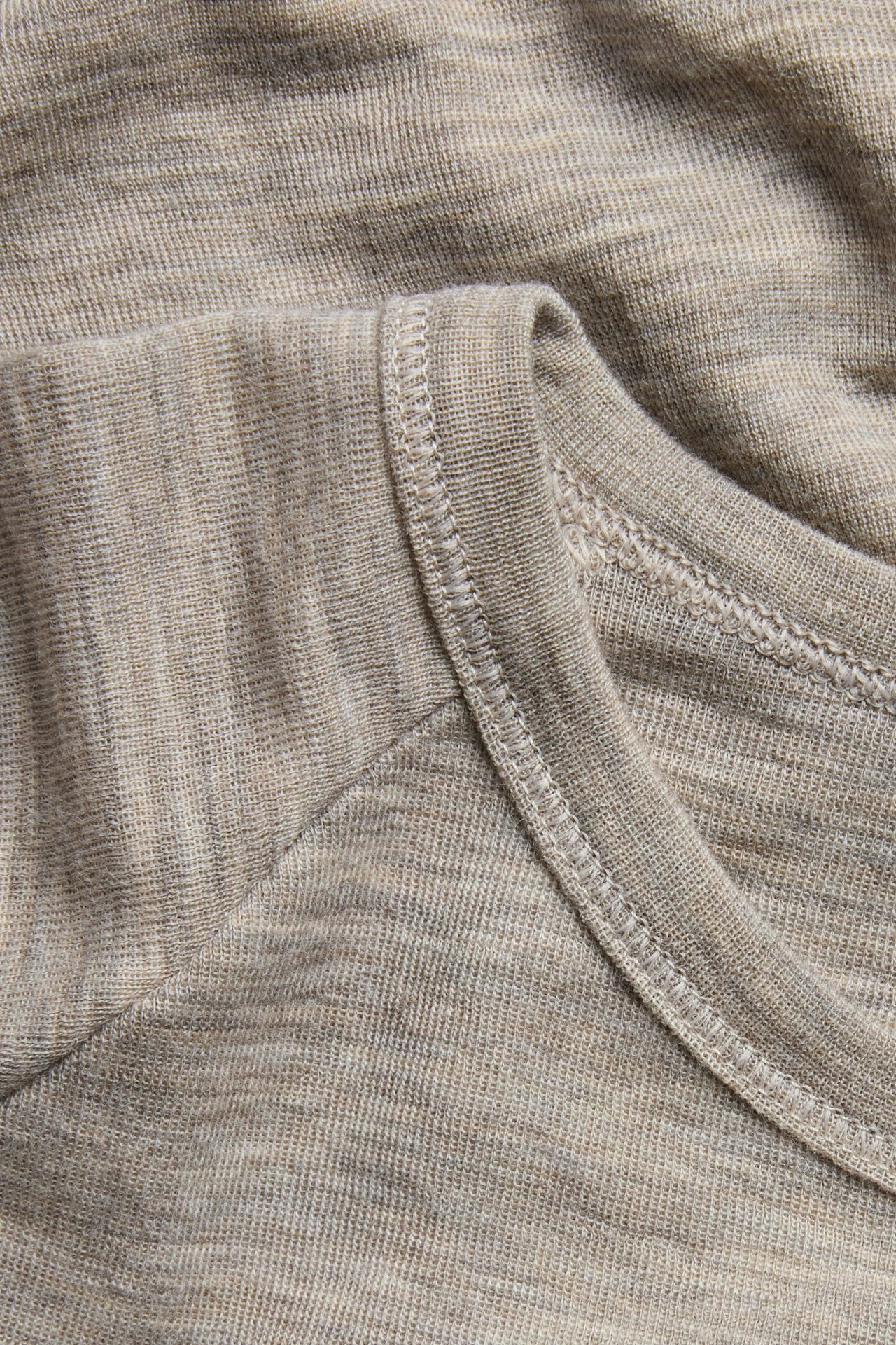 Zbliżenie beżowej melanżowej koszulki termicznej z wełny merynosów z widoczną prążkowaną fakturą i szwami.