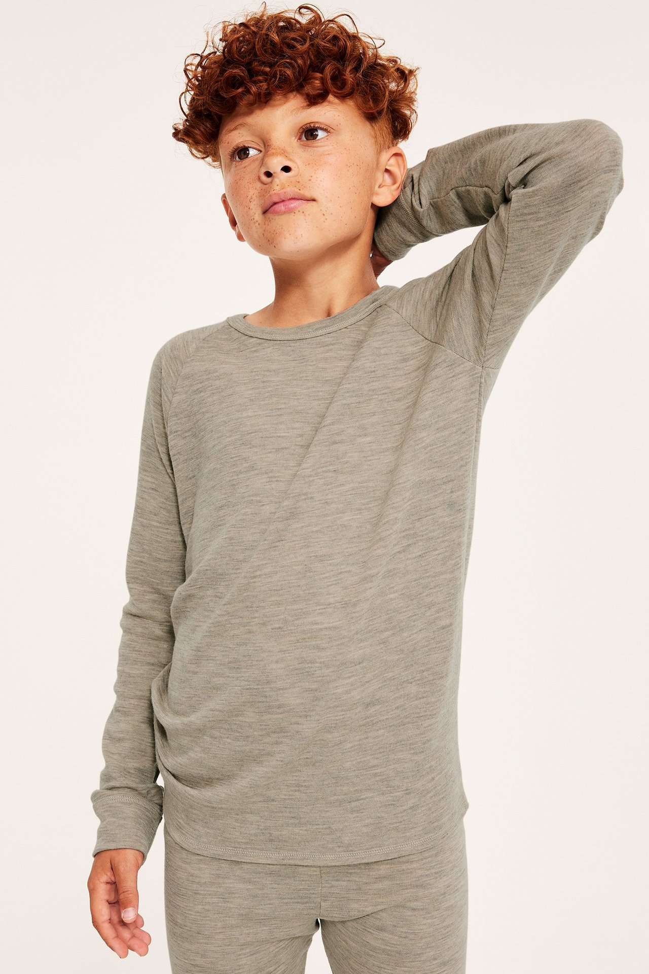 Dziecko w beżowej melanżowej koszulce termicznej z długim rękawem z merynosów i pasujących spodniach.
