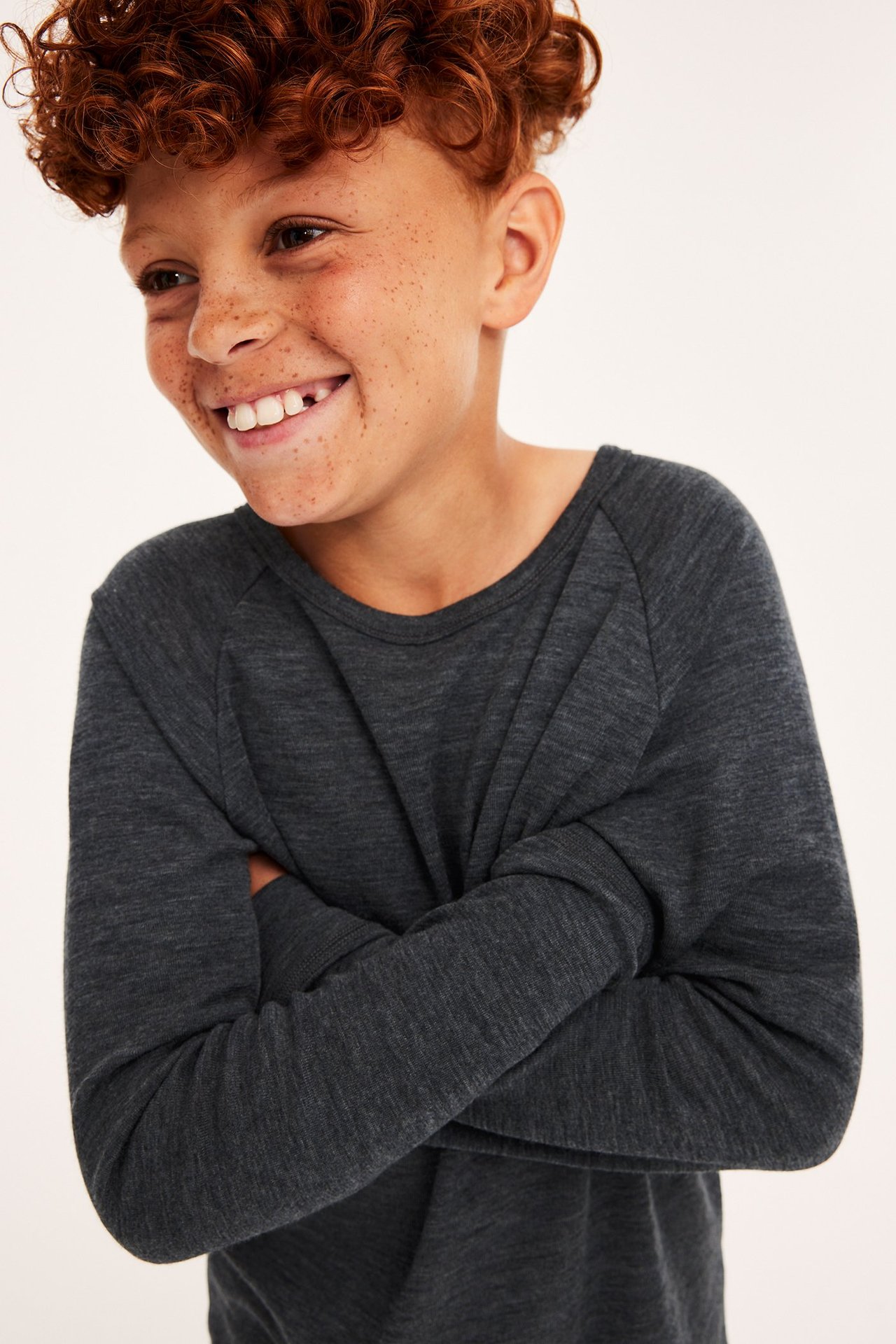 Närbild framifrån på ett leende barn i en mörkgrå melerad underställströja i merinoull.