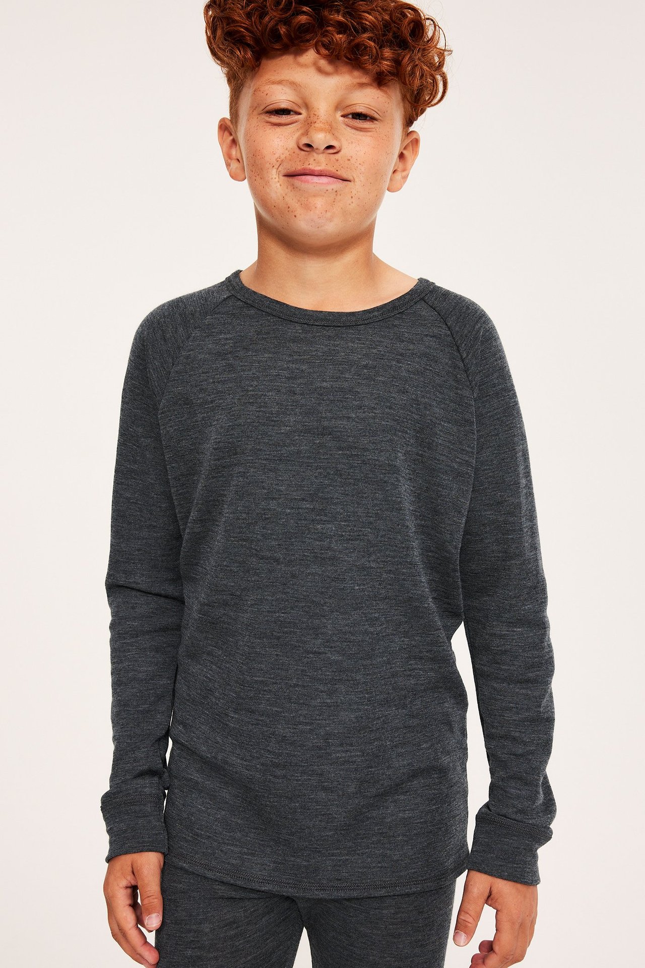Frontvy av ett barn i en mörkgrå melerad långärmad underställströja i merinoull och matchande byxor.